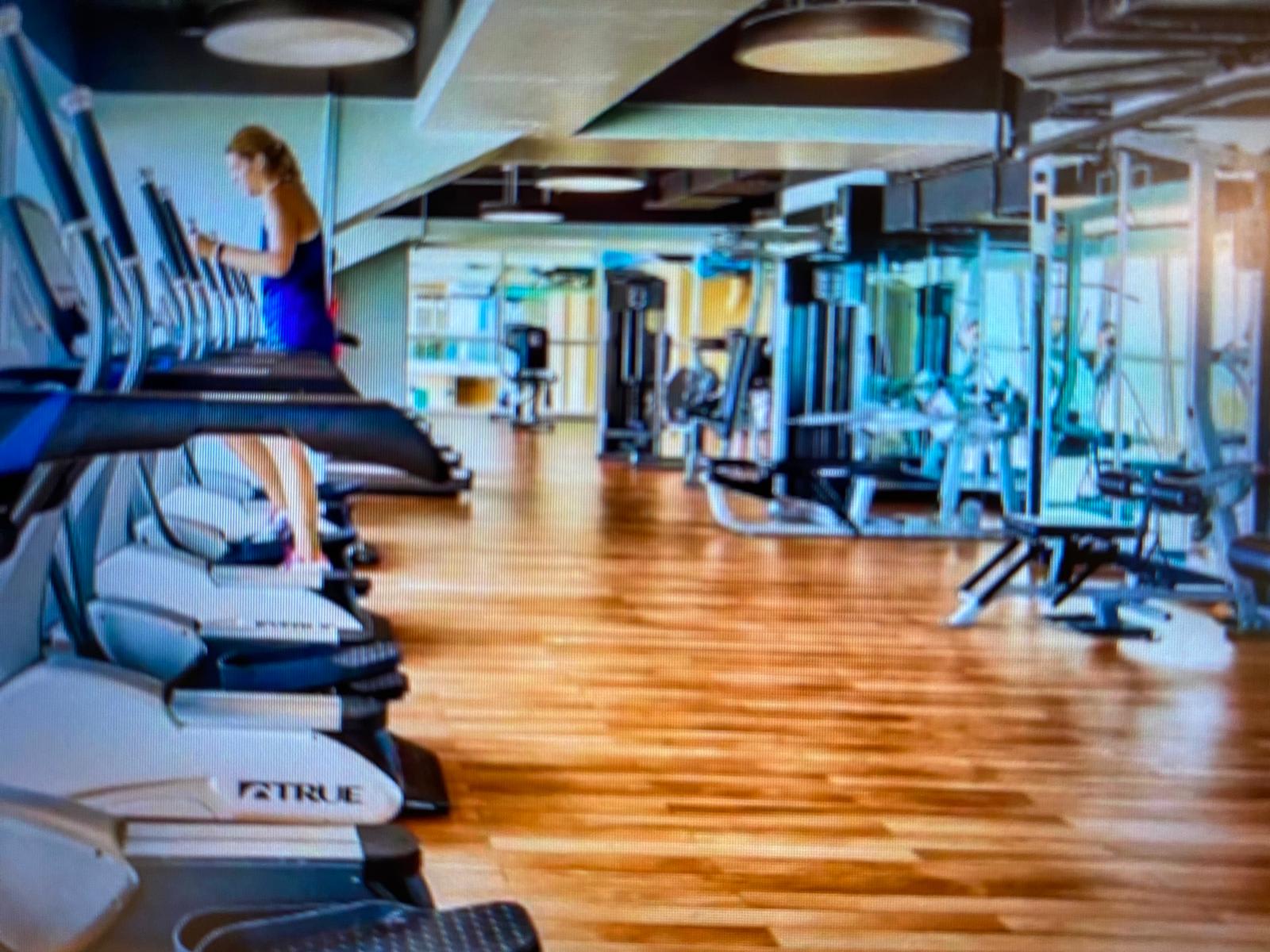 Splash 804E – Contemporary gym with cardio machines, weights, and a woman using an elliptical trainer.