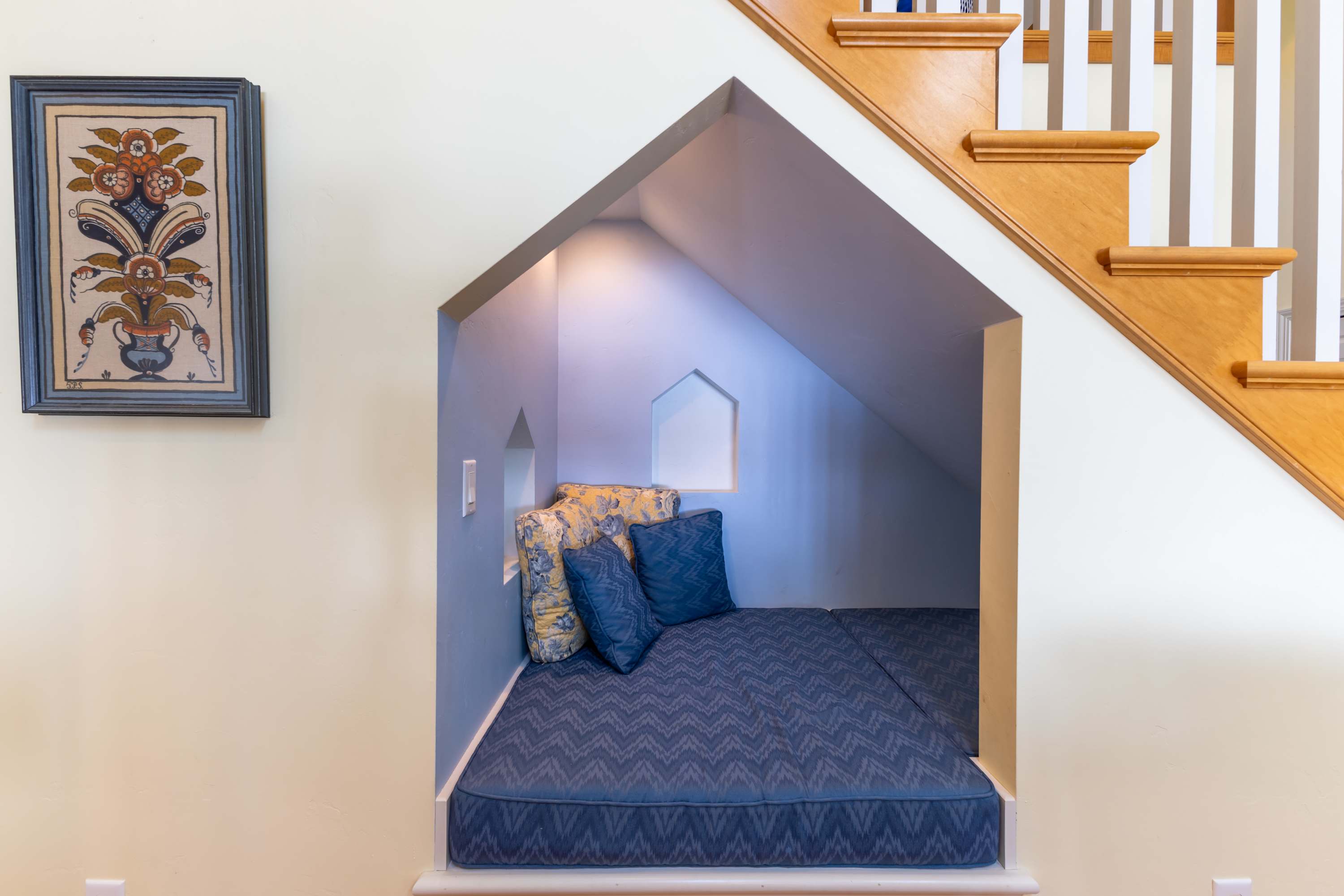Your magical hideaway awaits beneath the stairs, where cozy blue bedding and soft pillows create the perfect reading nook.