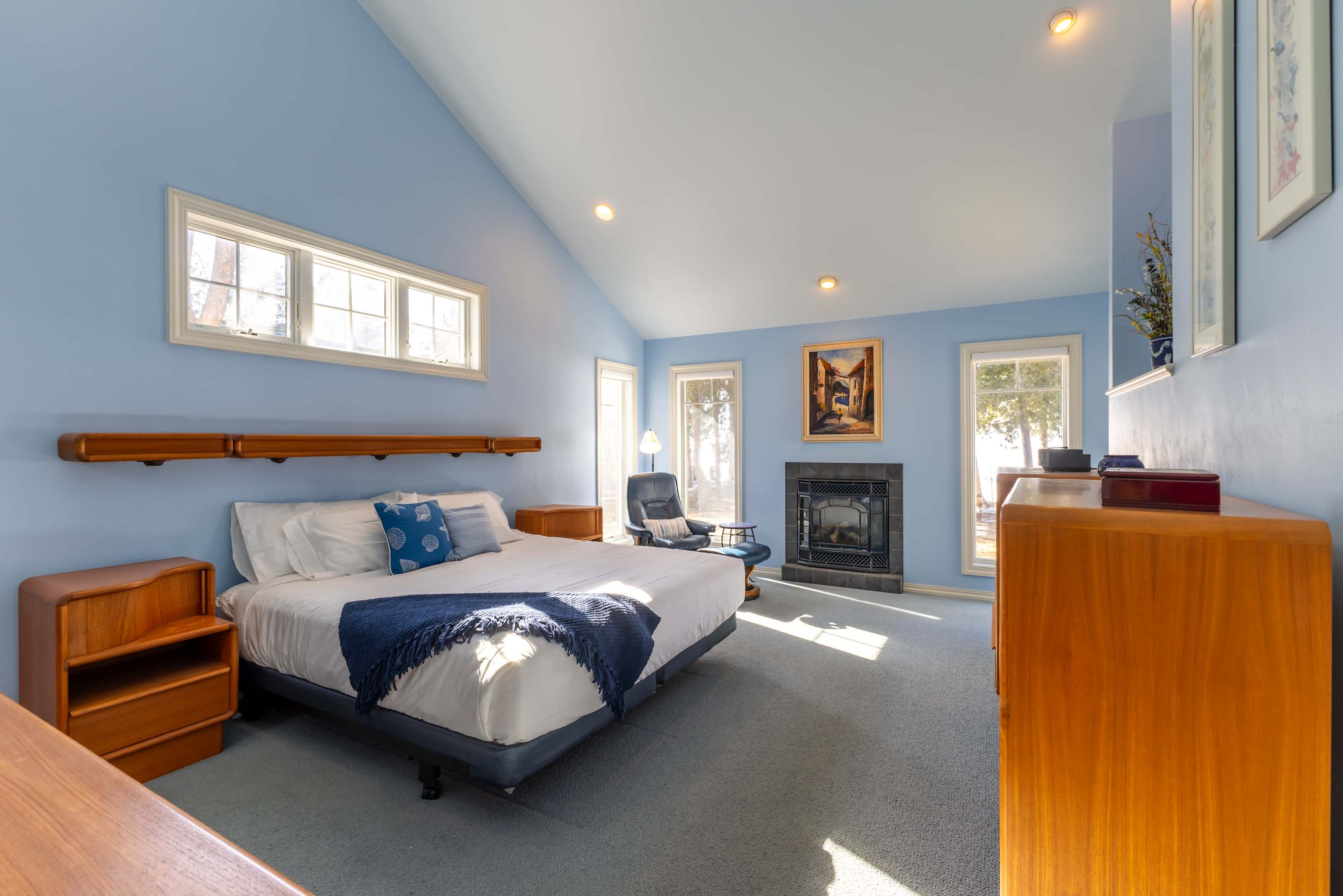 Just off the living room - Unwind in your serene Primary suite with warm wooden furnishings, soaring ceilings, and gas fireplace, perfect for peaceful relaxation.