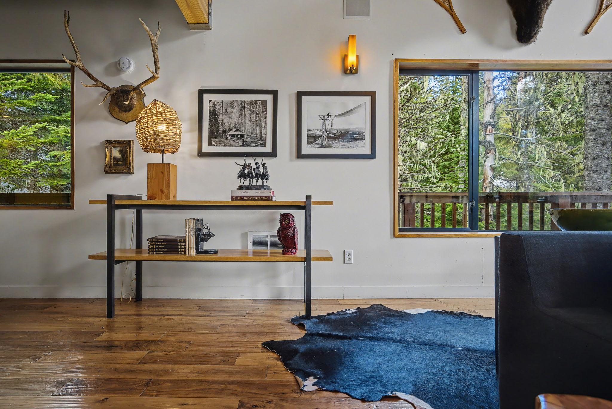 Cozy corner of the living room featuring a console table with decorative items and framed artwork on the wall. Large windows provide ample natural light and immersive forest views.