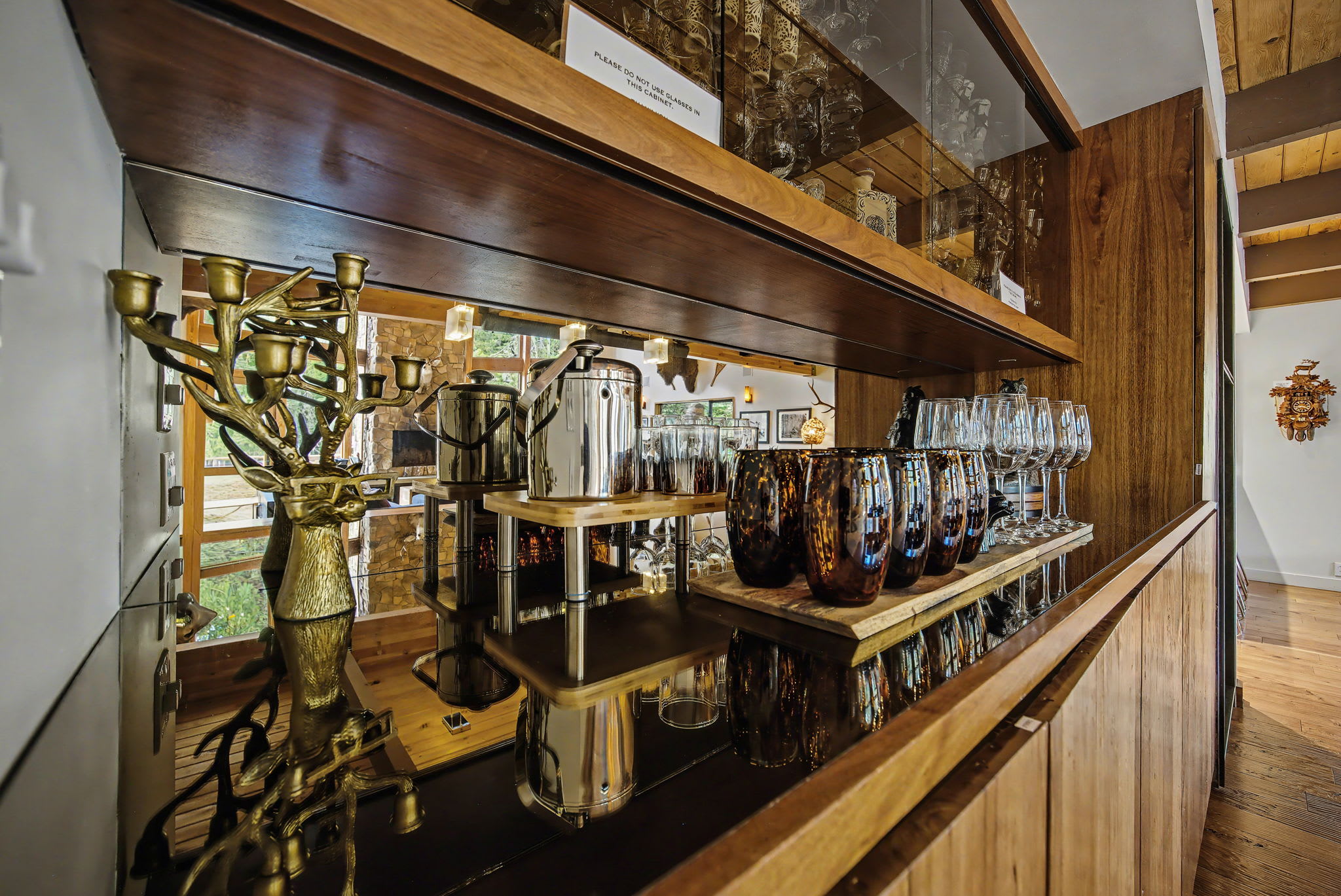A detailed shot of the built-in bar area, featuring mirrored shelves stocked with glassware and bottles, and a polished dark countertop. Decorative items like a golden candelabra add to the sophisticated rustic ambiance.