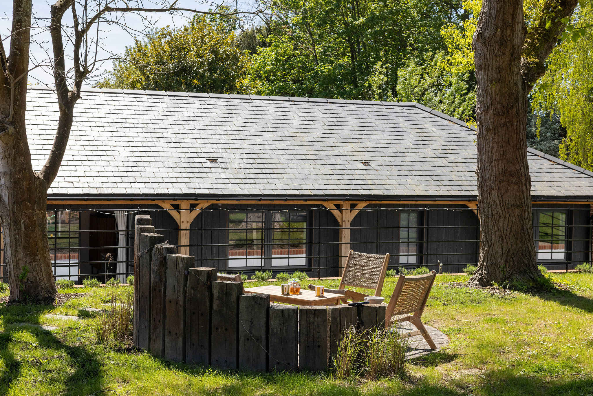 Sip morning tea beneath tall trees, with rustic seating tucked beside a tranquil countryside lodge.