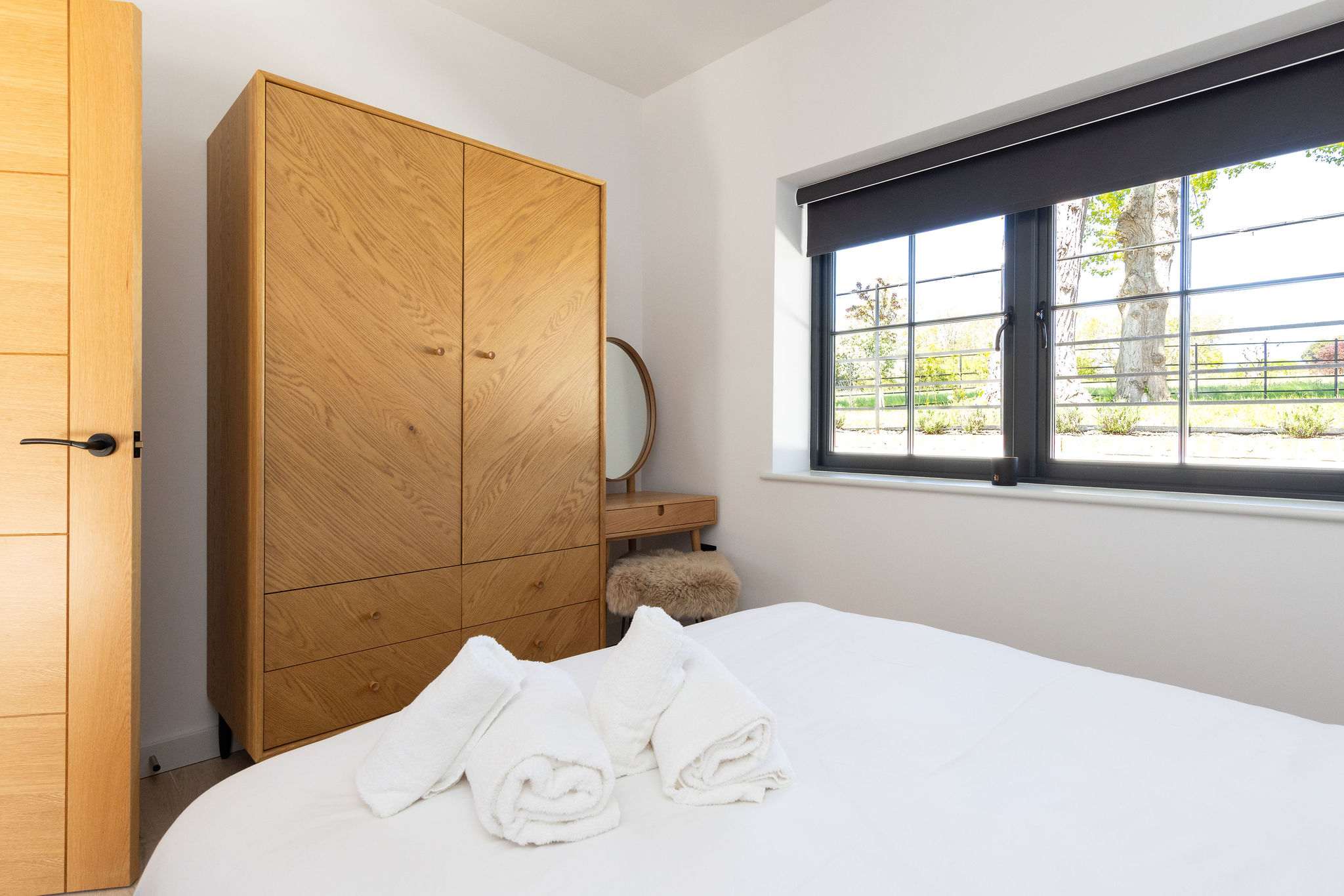 Store luggage easily in the serene bedroom, featuring warm wood finishes and soft morning light.
