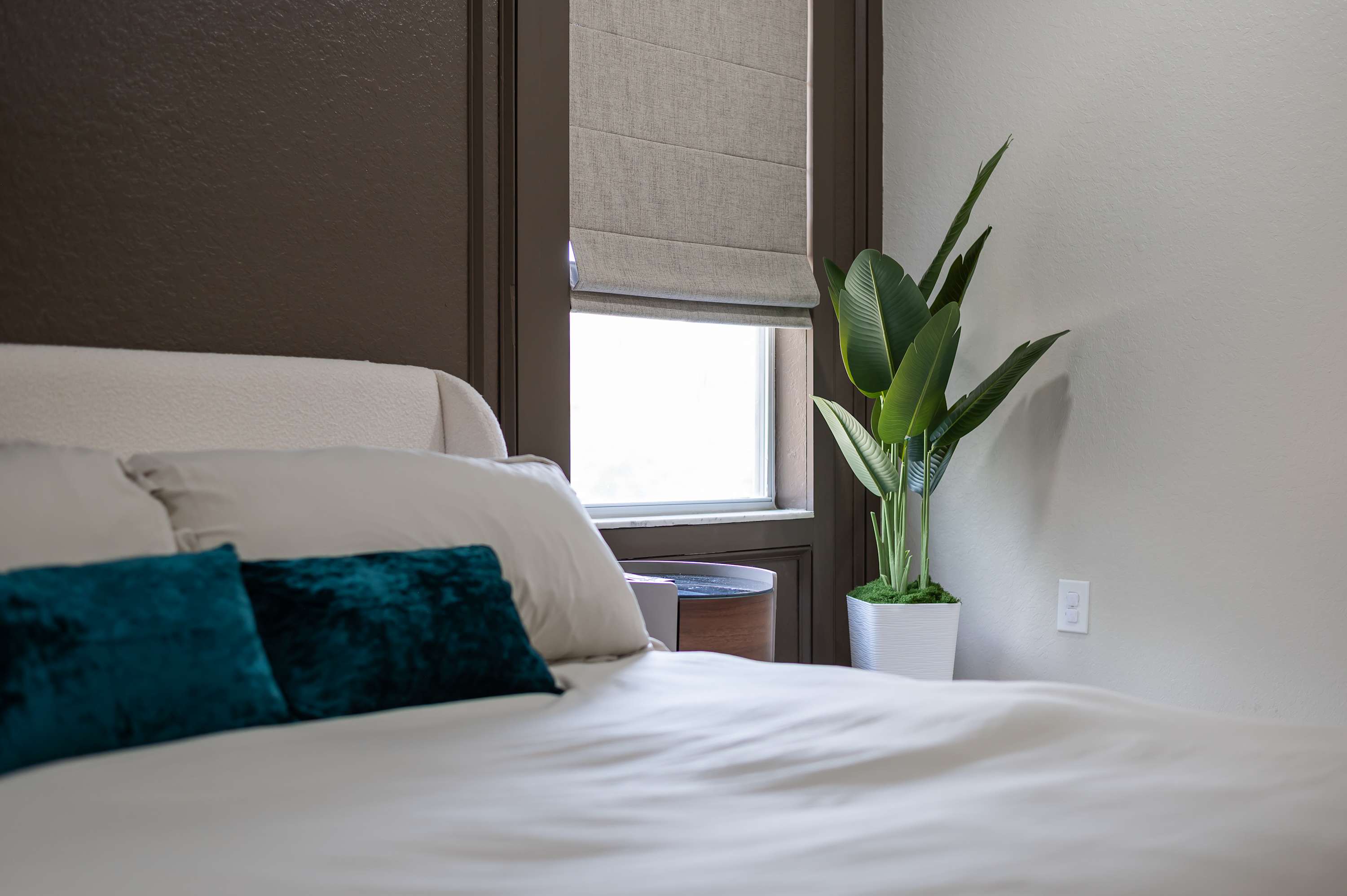Serene bedroom corner w/ soft linens, plant accents & window light