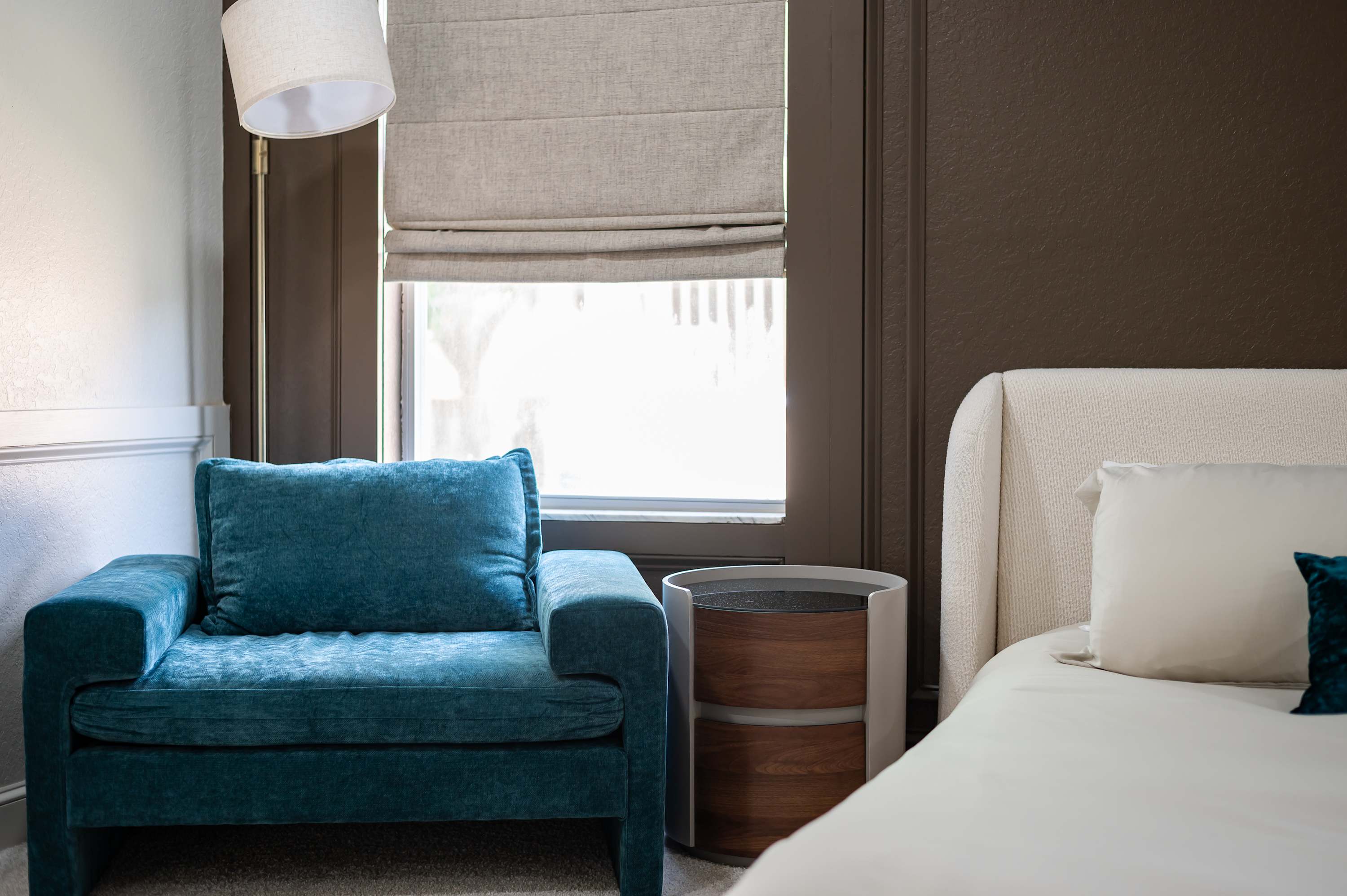 Cozy master bedroom corner w/ accent chair, soft lighting & plush bedding