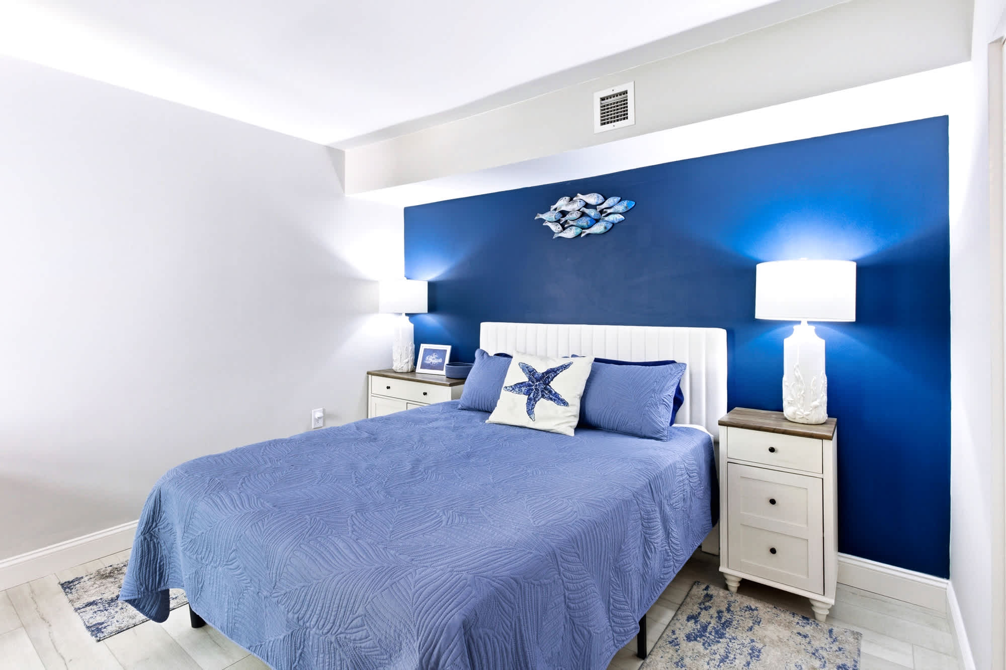 Drift off in the guest bedroom: queen bed dressed in plush linens, calming blue-and-white palette, and a starfish accent pillow for good measure.