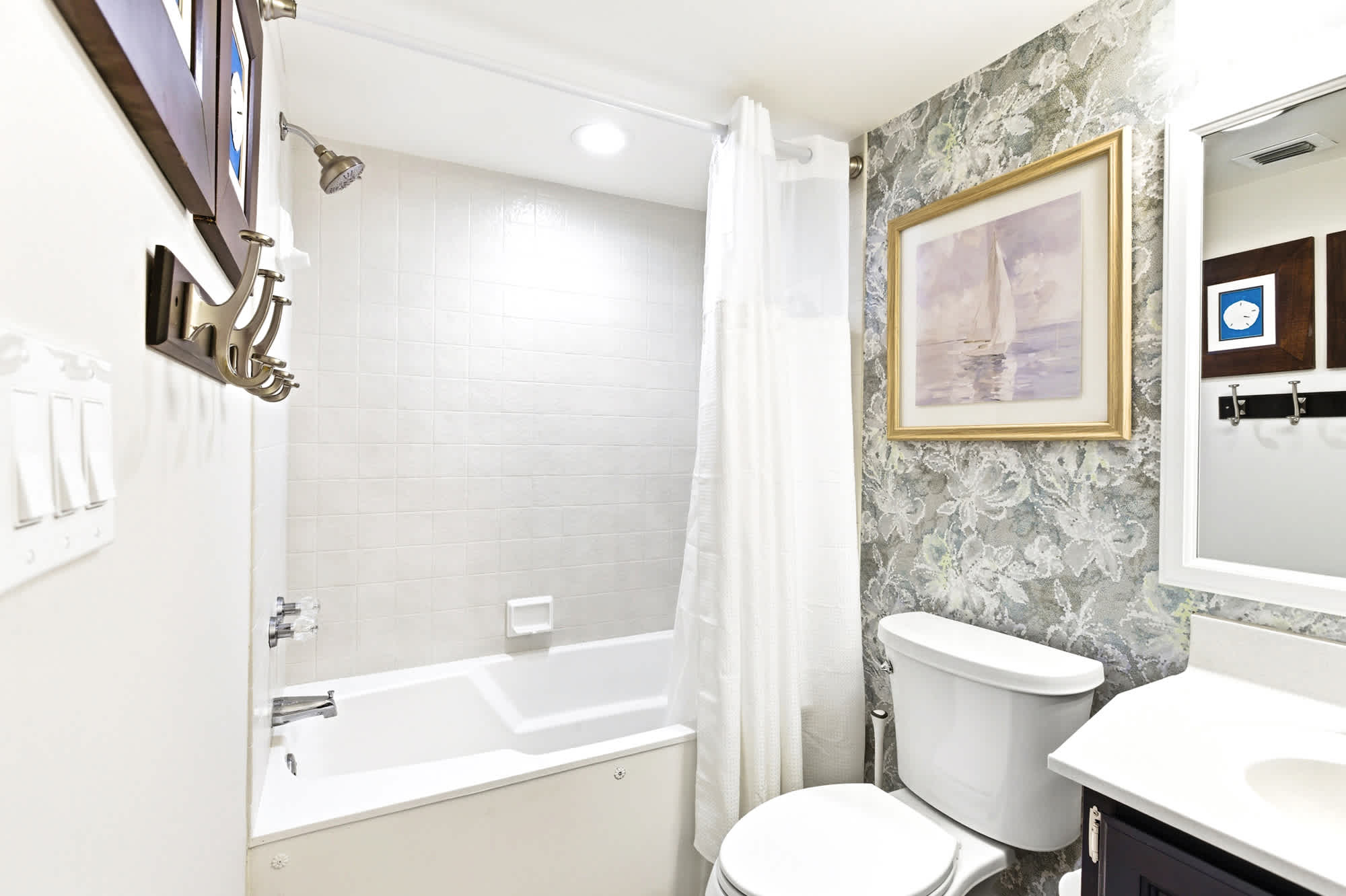 Updated guest bath with a deep tub/shower combo, fresh white tile, and a sailboat print - beach-inspired and totally relaxing.