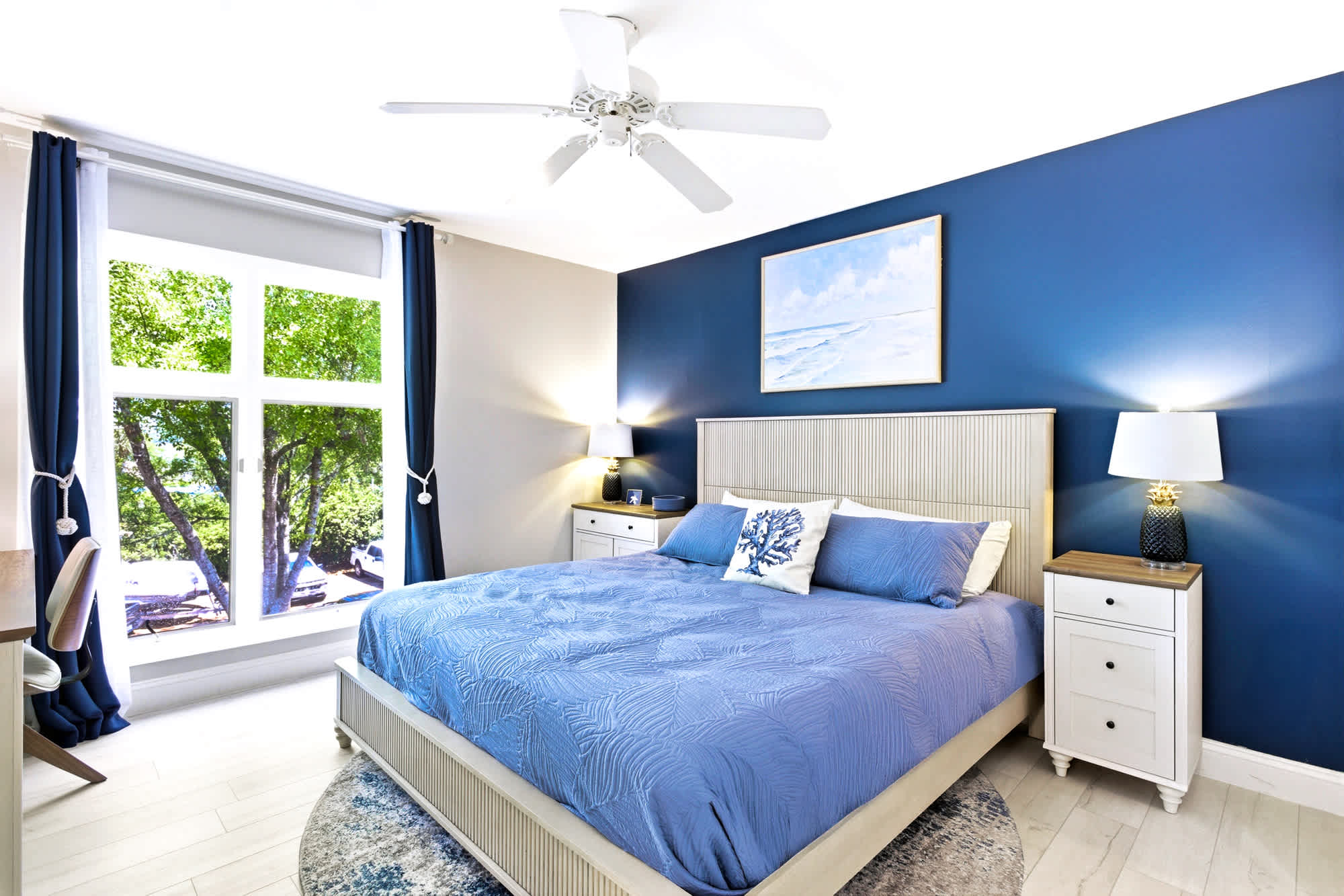King bed dressed in crisp linens against a calming blue accent wall, with a starfish pillow and shell wall art - a peaceful place to land at the end of the day.