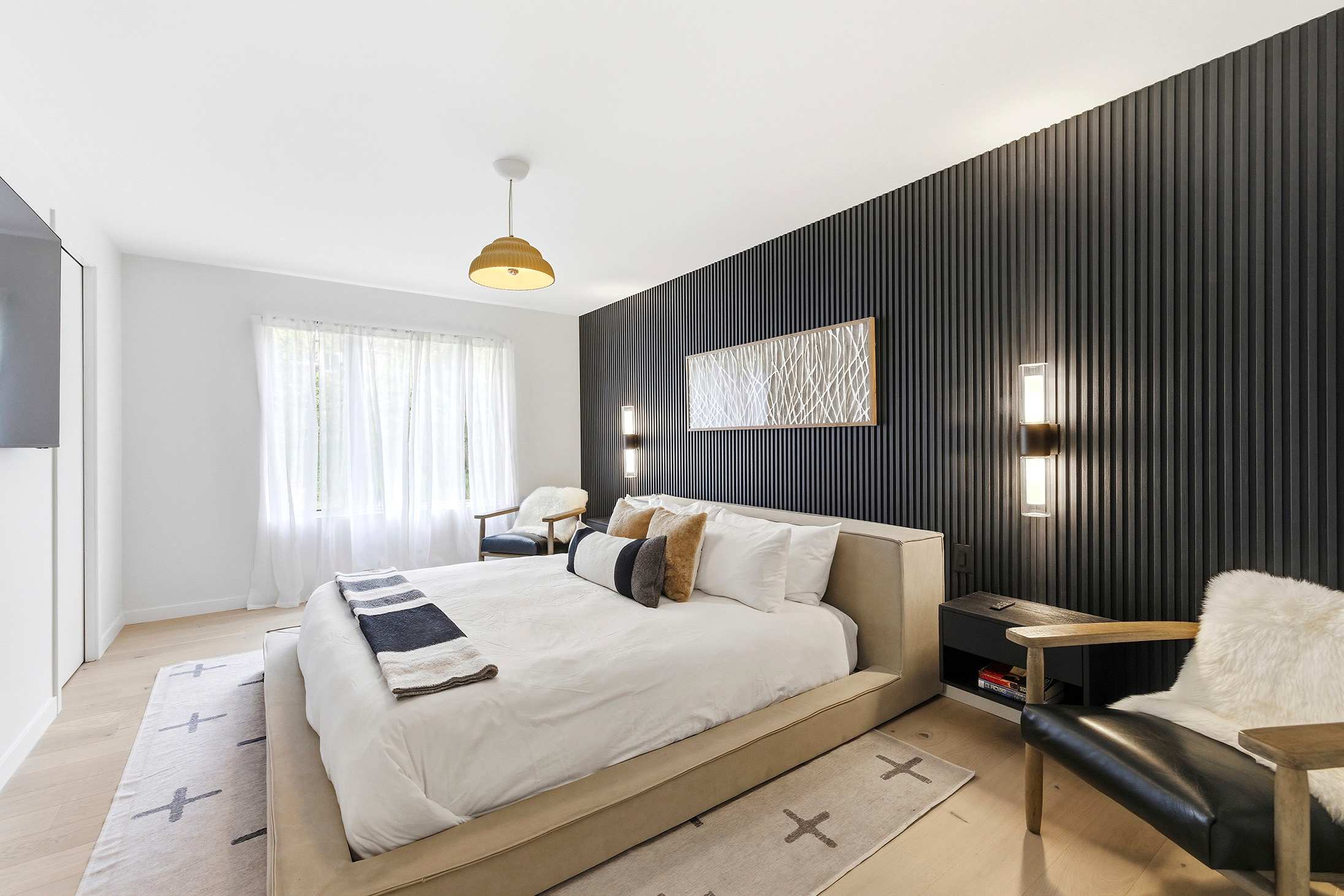 Crisp white linens and warm natural wood meet a bold charcoal slat wall in this contemporary primary bedroom.