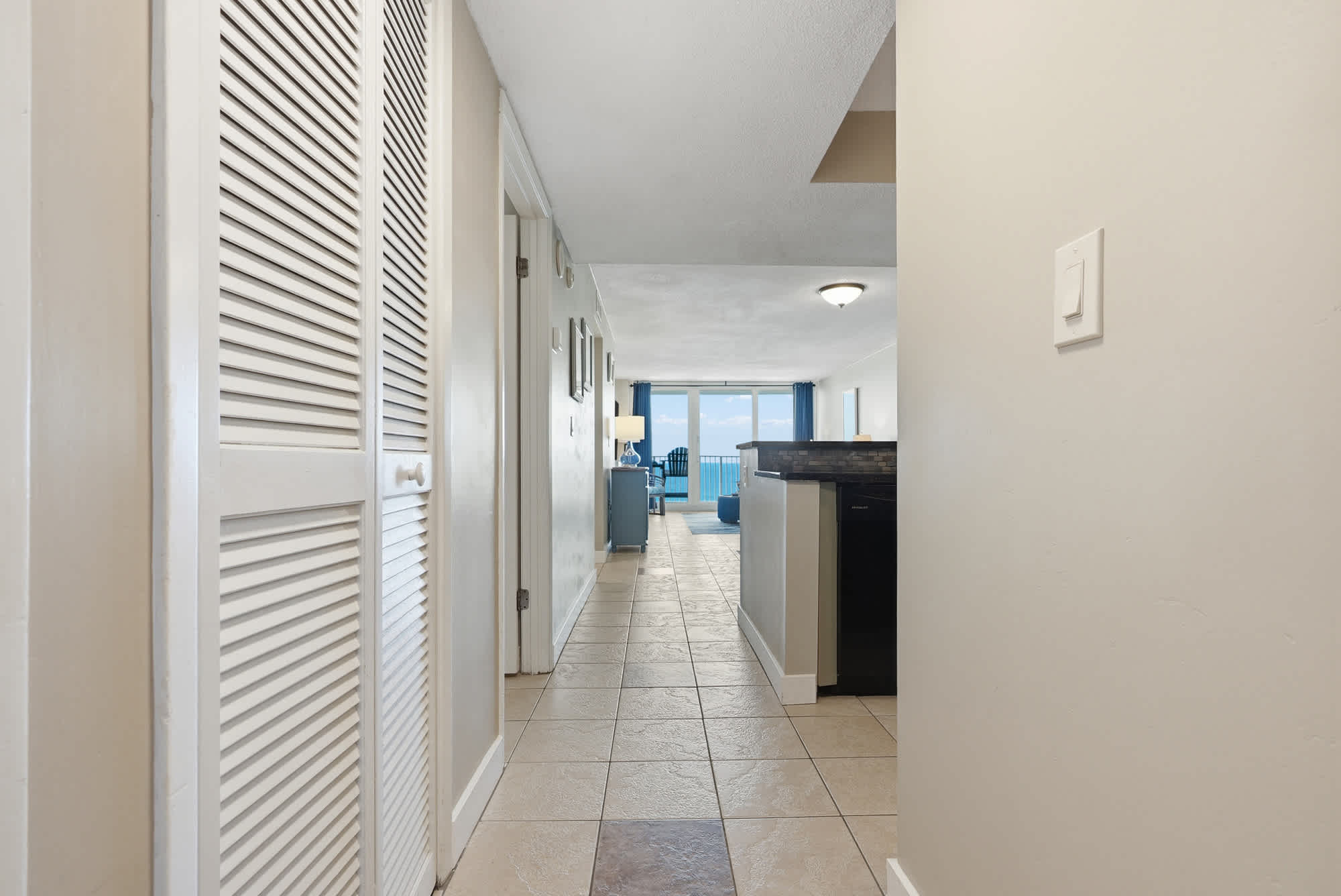 Dunes E1702 – Hallway leading to a bright living area with ocean view and tiled floor.