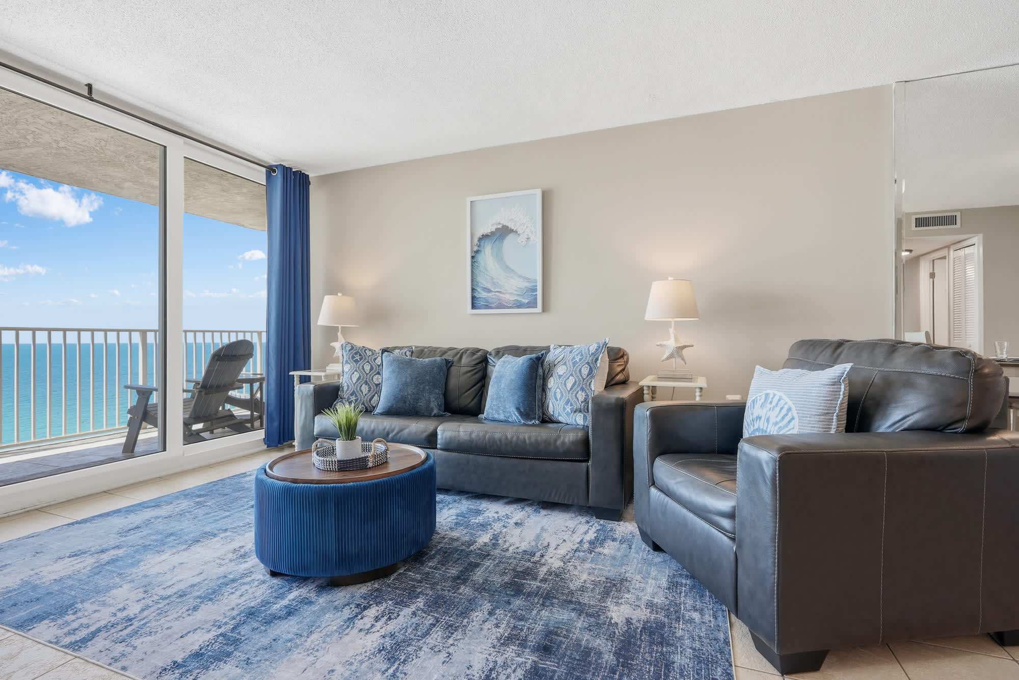 Dunes E1702 – Living room with ocean view, blue furniture, large windows, and decorative rug.
