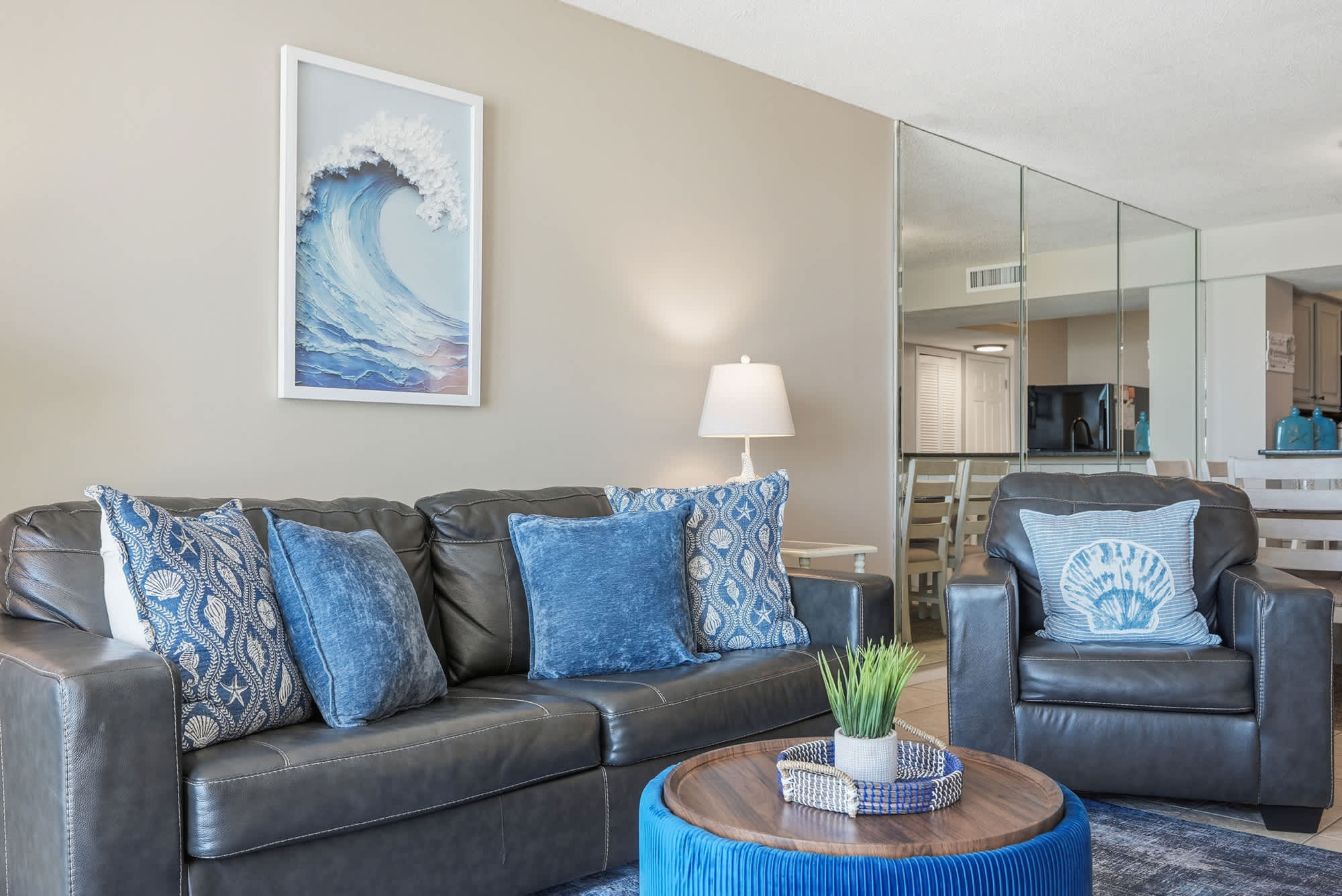 Dunes E1702 – Living room with leather couch, decorative pillows, and coffee table; art piece of a wave on the wall.