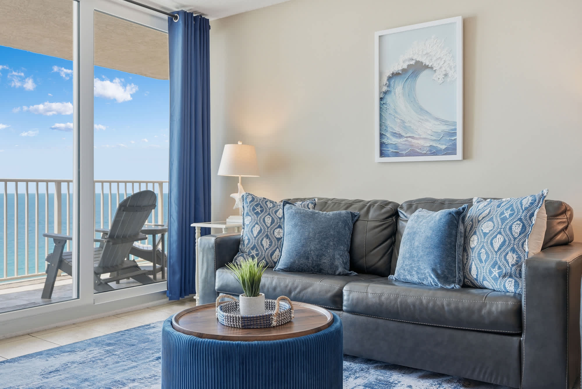 Dunes E1702 – Living room with a gray sofa, decorative pillows, ocean view balcony, and blue accent features.