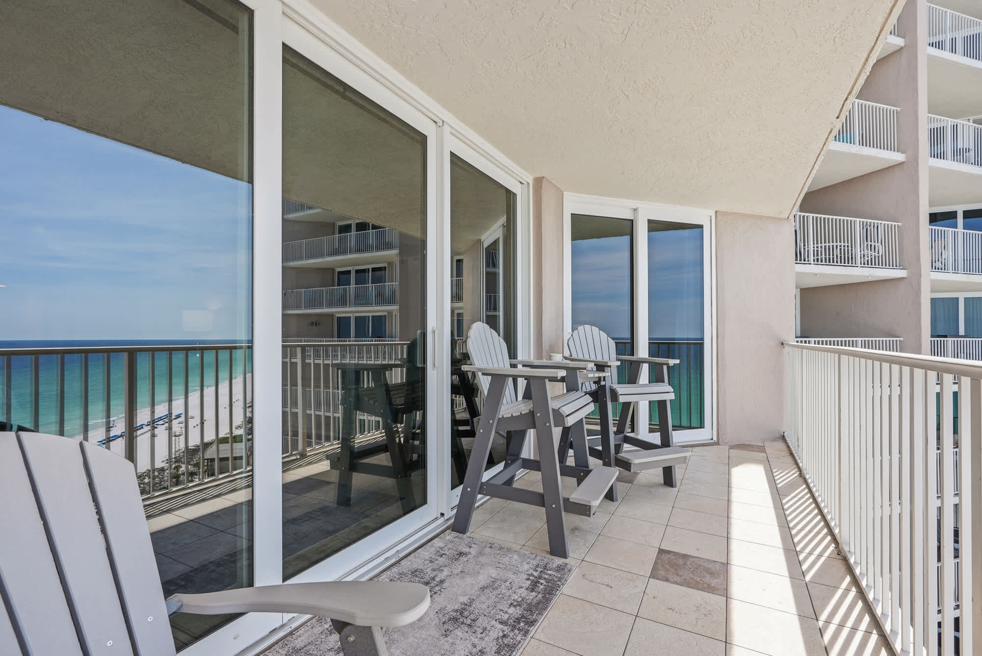 Dunes E1702 – Balcony with two chairs overlooking the beach and ocean, large windows reflecting the view.