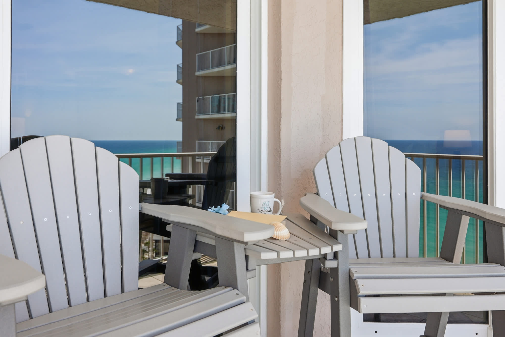 Dunes E1702 – Two gray Adirondack chairs on a balcony overlooking the ocean.