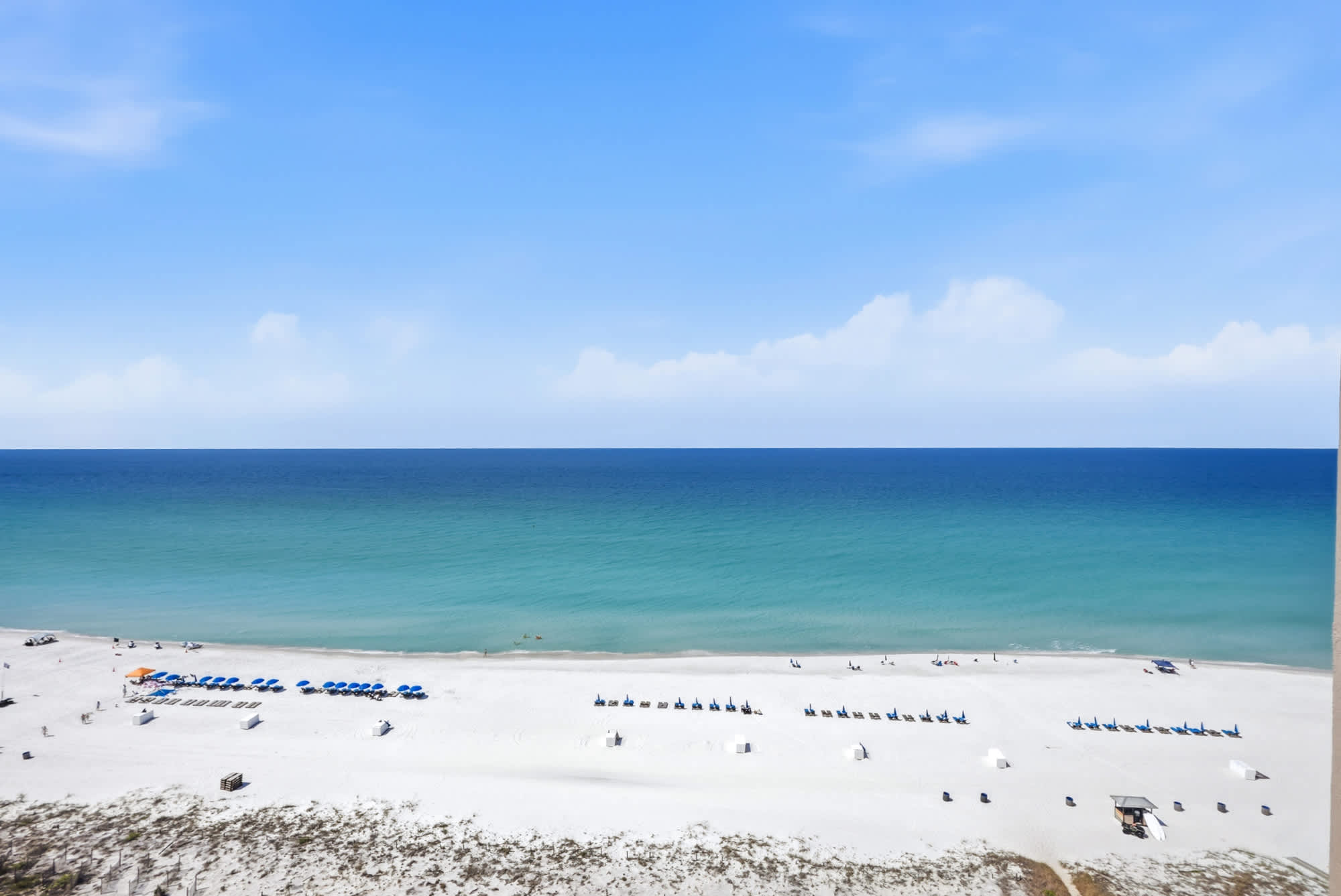 Dunes E1702 – Ocean view from a high-rise, featuring a sandy beach with blue umbrellas and chairs.