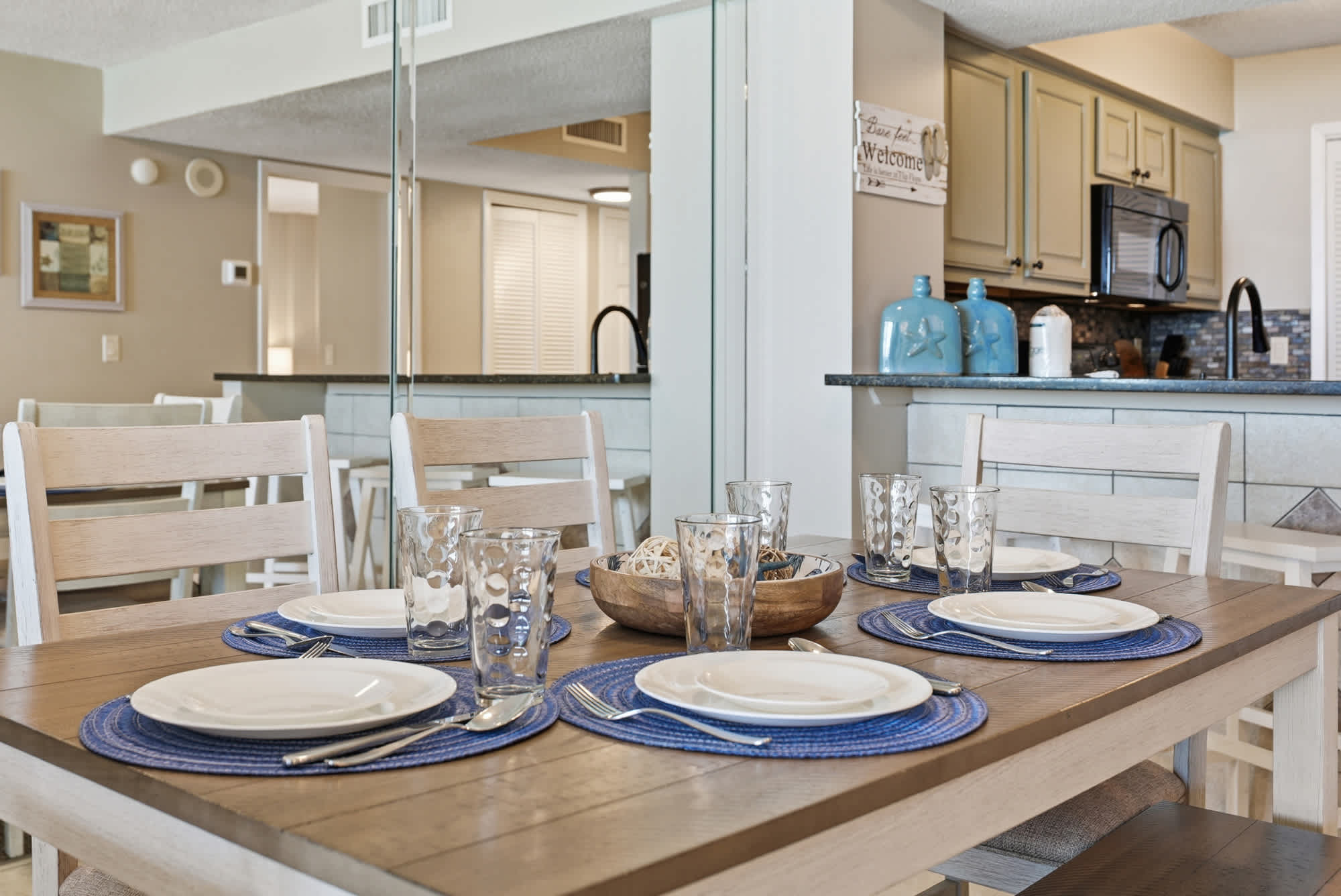 Dunes E1702 – Dining area with a wooden table set for six and a view of a kitchen.