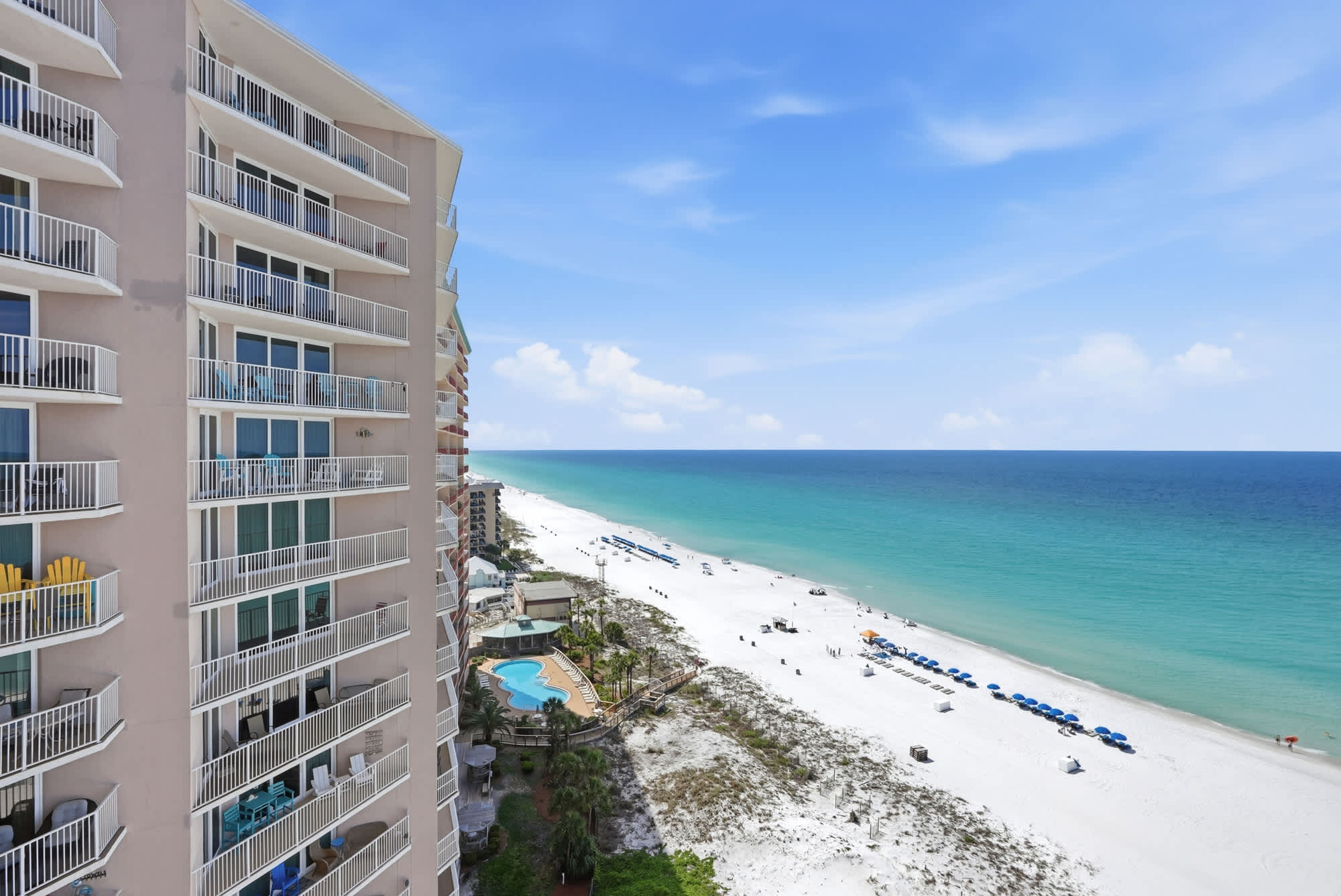 Dunes E1702 – View of beach with umbrellas, swimming pool, and ocean from a high-rise balcony.