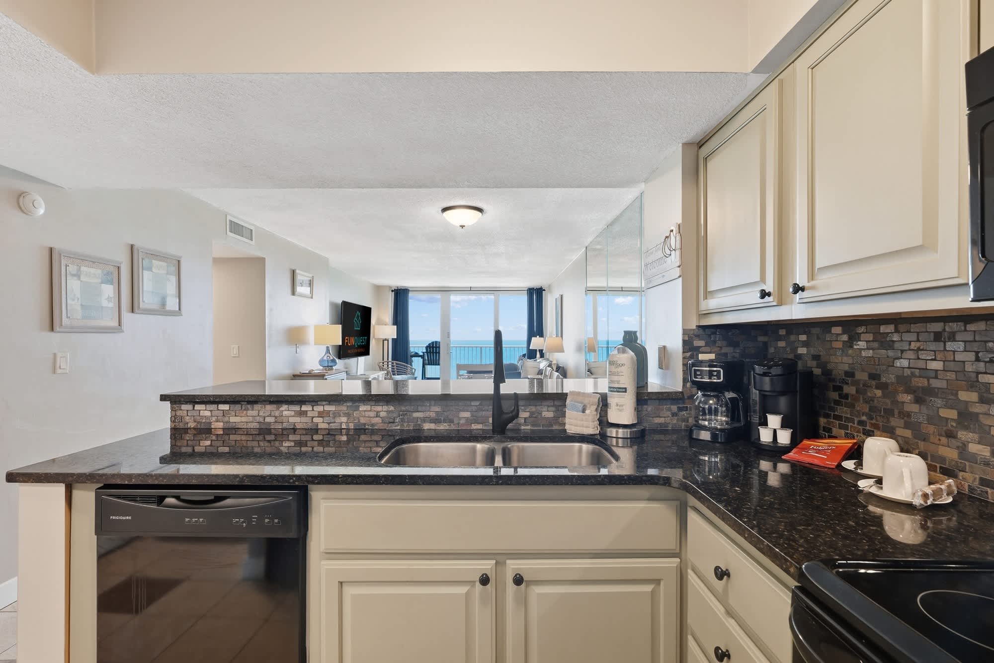 Dunes E1702 – Kitchen with granite countertop, black appliances, and ocean view through windows.
