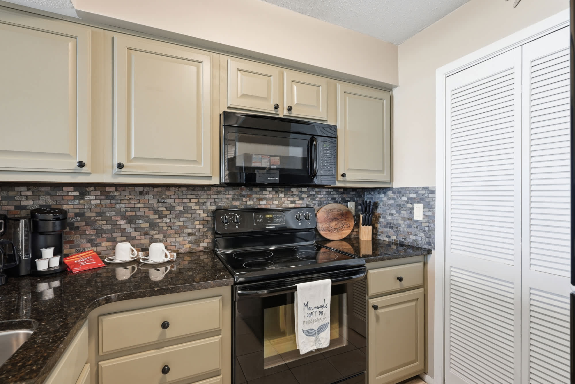 Dunes E1702 – Kitchen featuring black appliances, granite countertops, and mosaic backsplash.