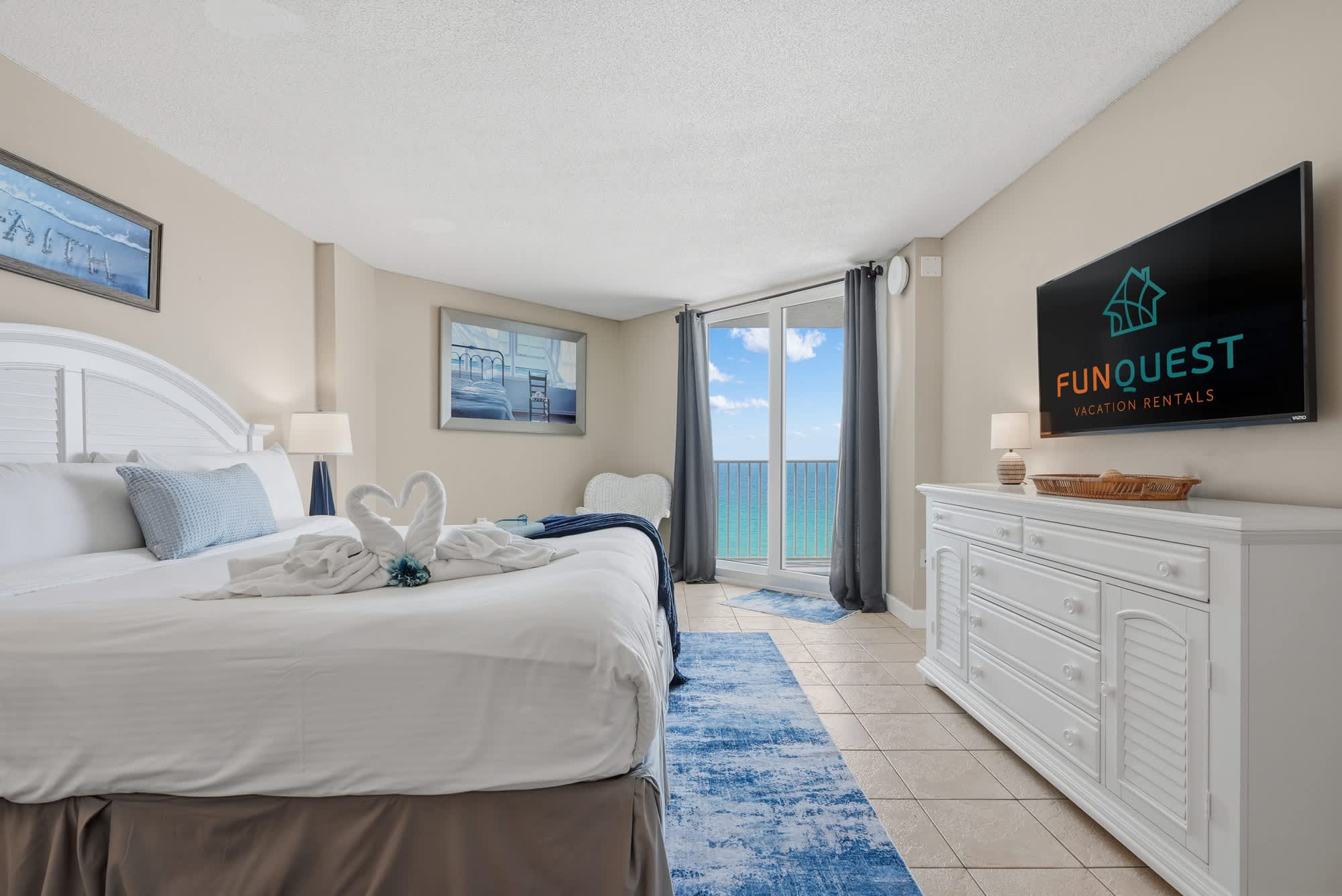 Dunes E1702 – Bedroom with a large bed, balcony view of the ocean, and a flat-screen TV.