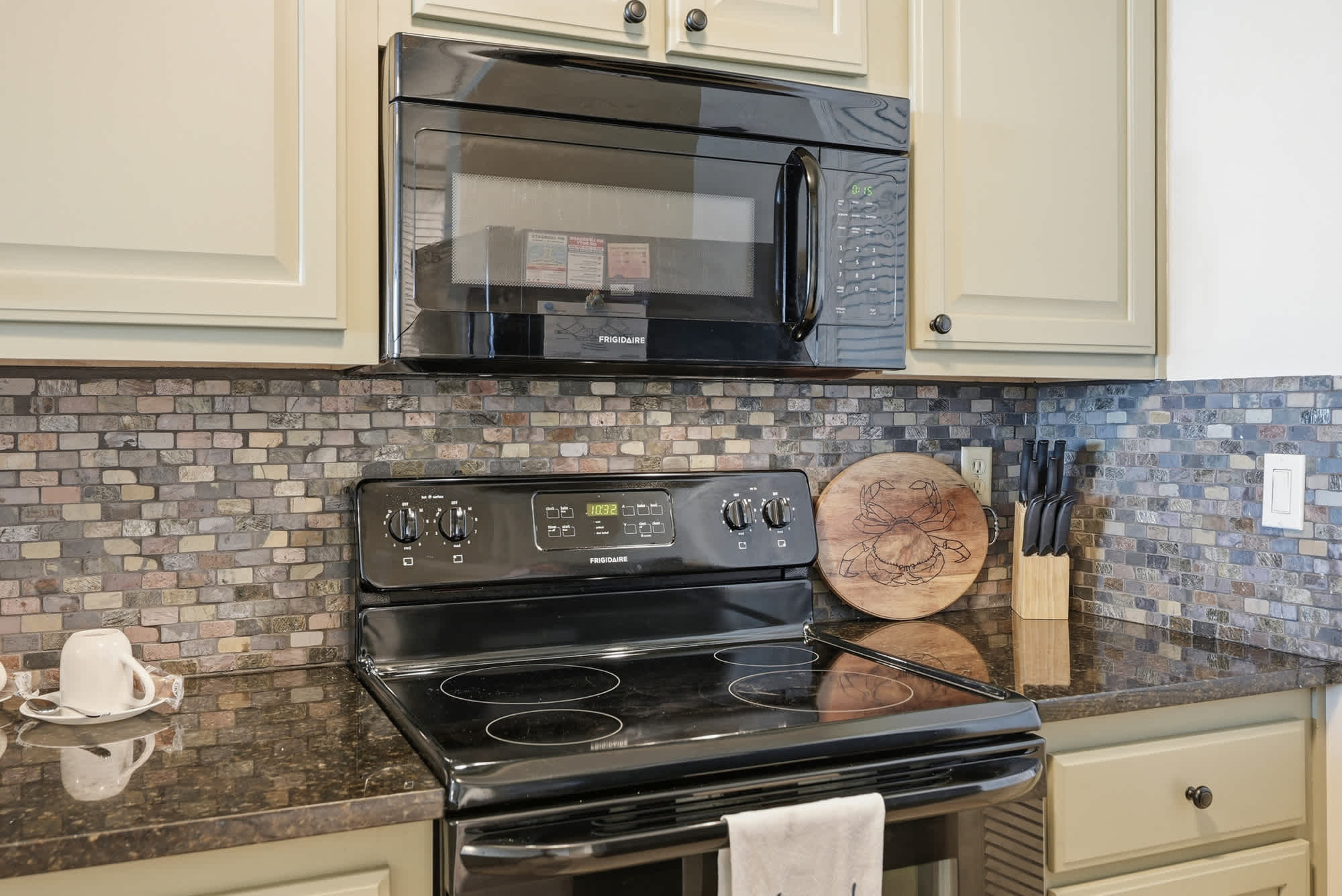 Dunes E1702 – Kitchen area featuring a black stove, microwave, and decorative tile backsplash.