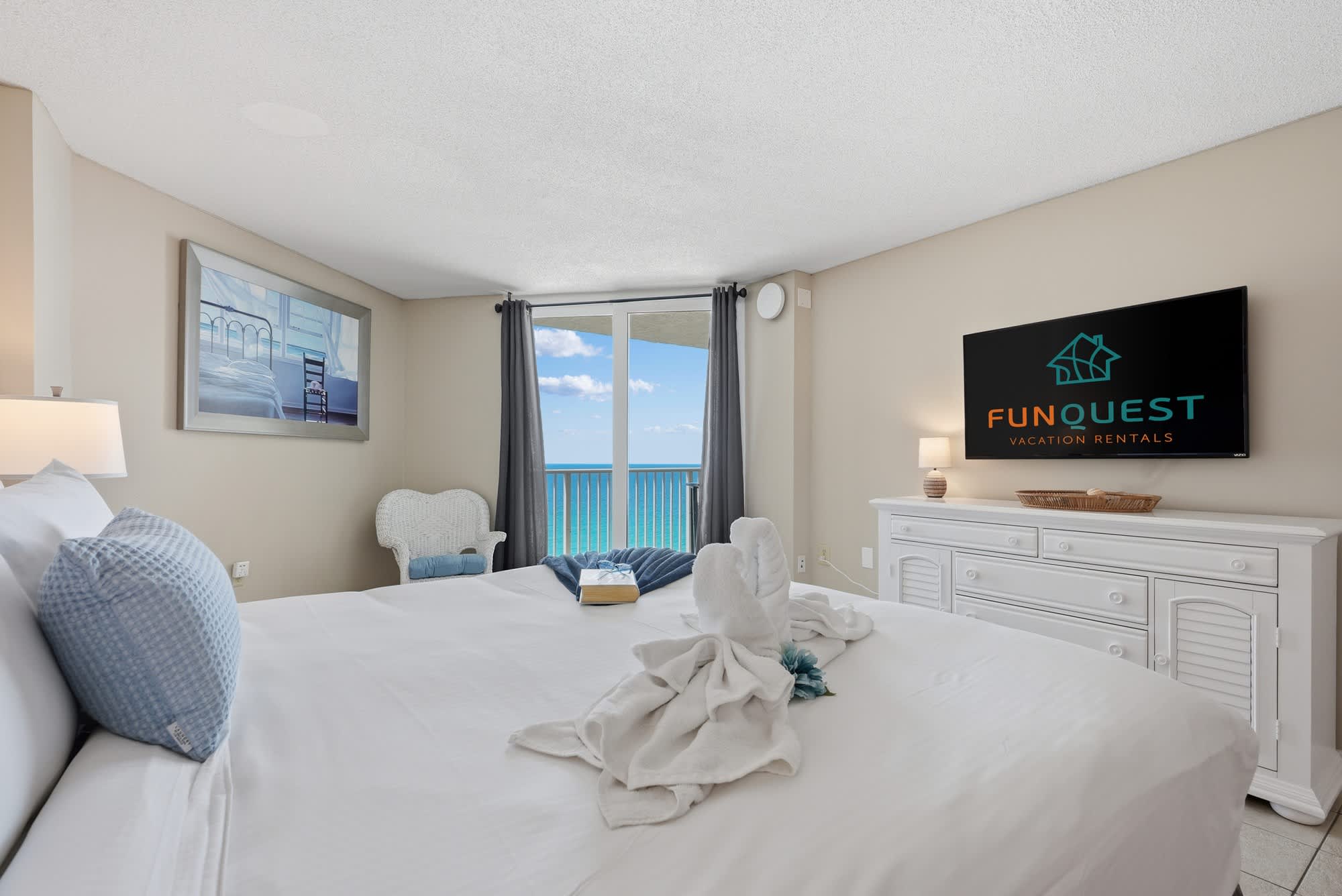 Dunes E1702 – Cozy bedroom with a balcony view of the ocean, white furniture, and decorative towels.