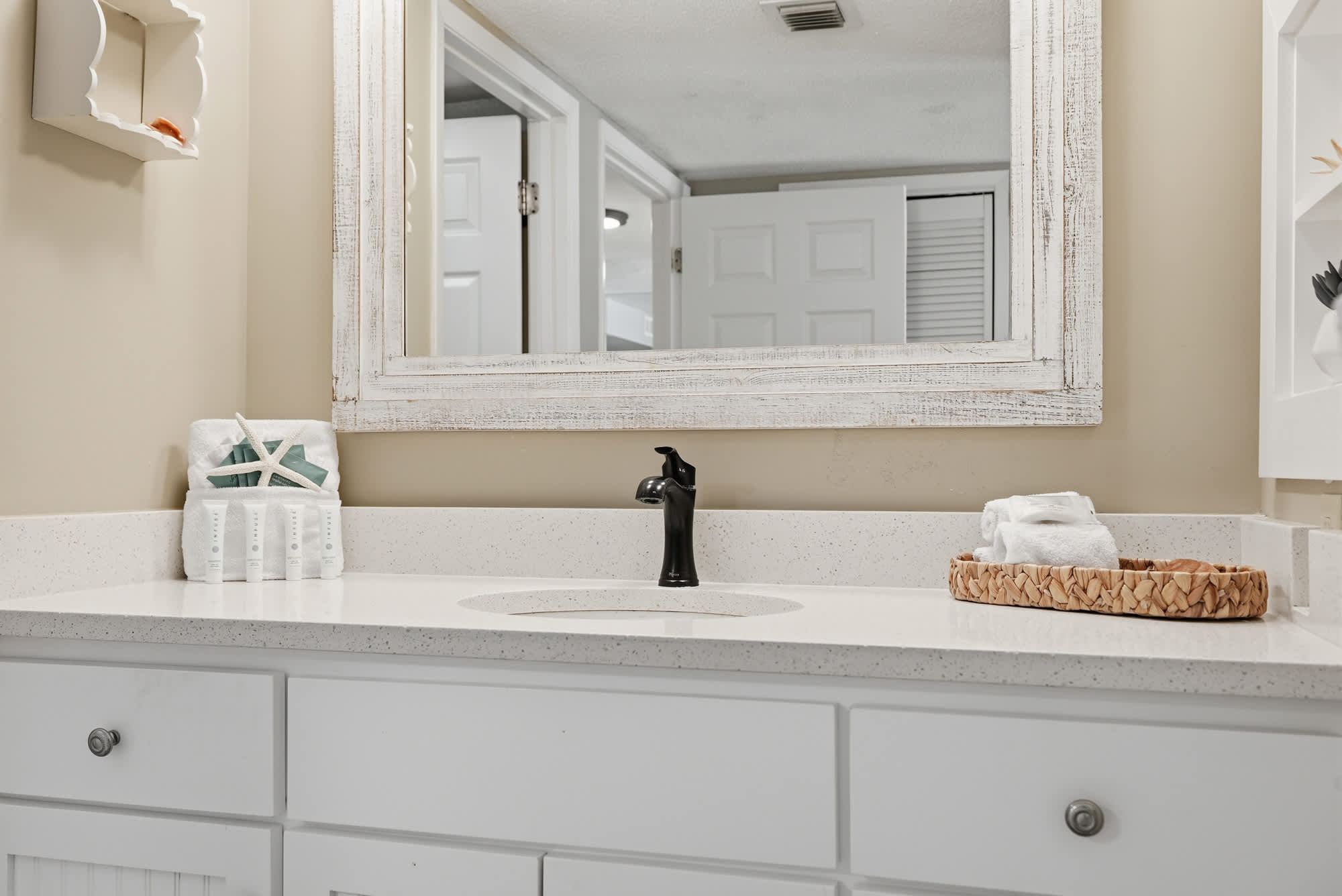 Dunes E1702 – Bright bathroom with white cabinetry, mirror, and modern black faucet on a stone countertop.