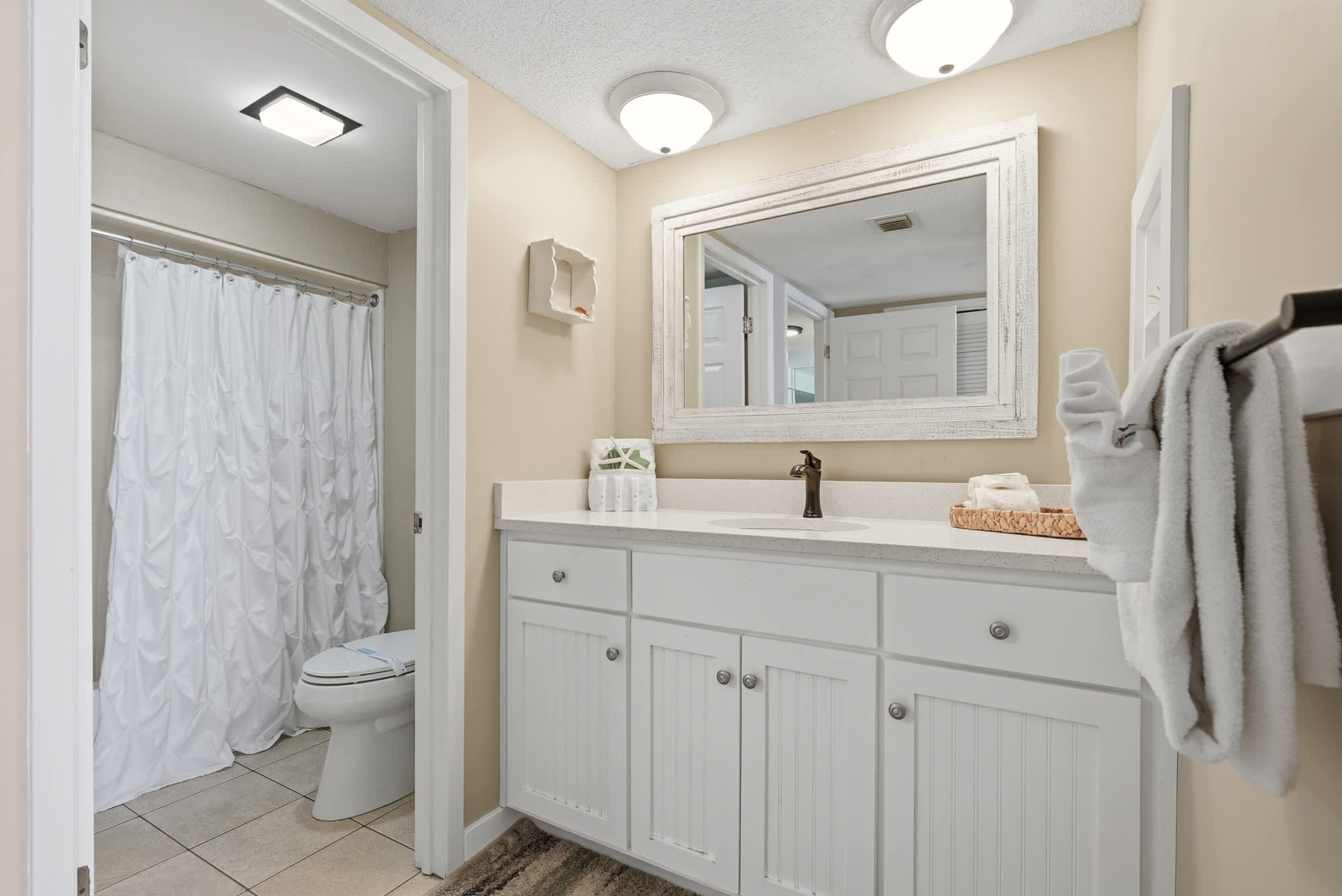 Dunes E1702 – Bathroom with sink, white cabinets, mirror, shower curtain, and towels.