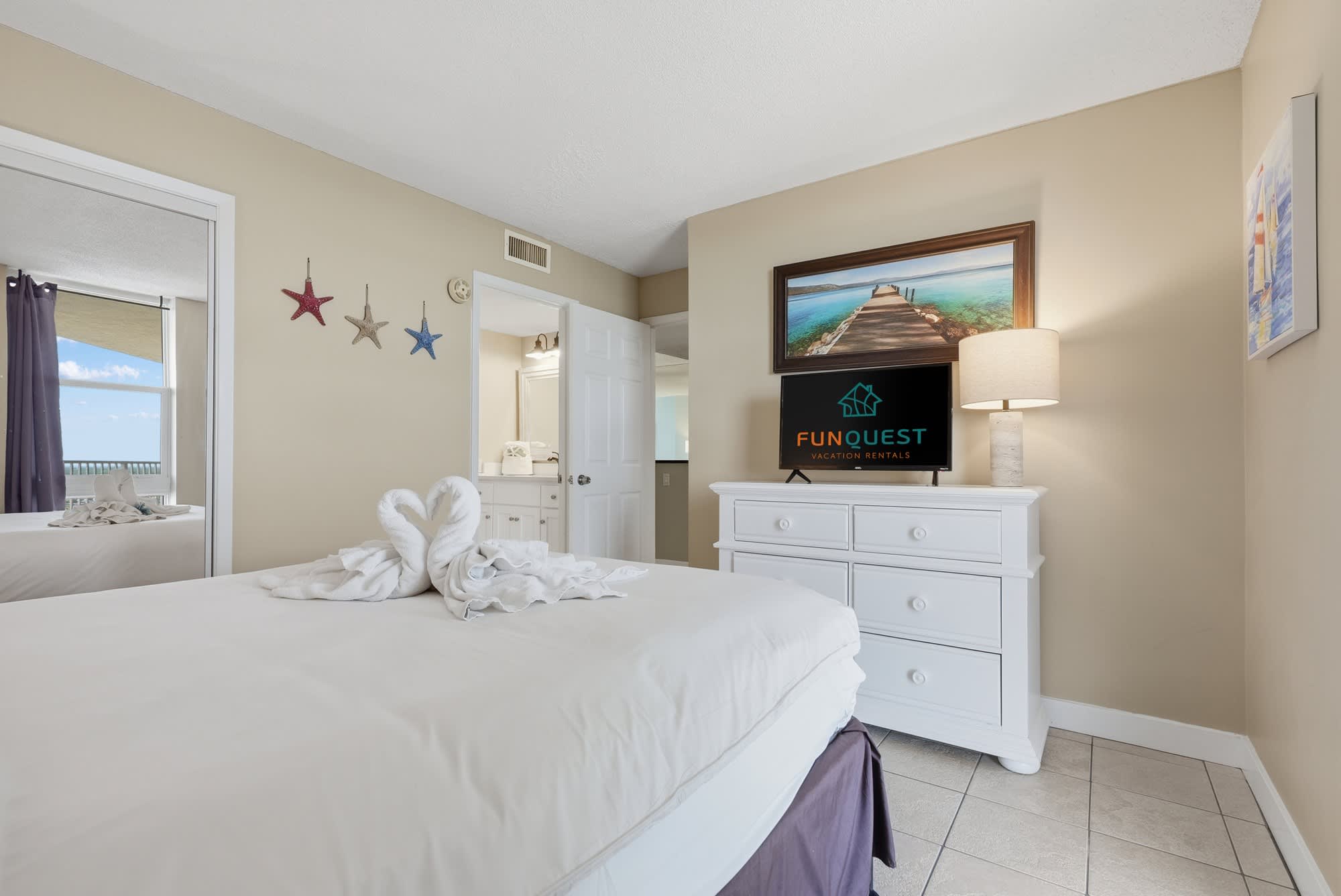 Dunes E1702 – Cozy bedroom with a white bed, decorative stars, television, and a door leading to a bathroom.