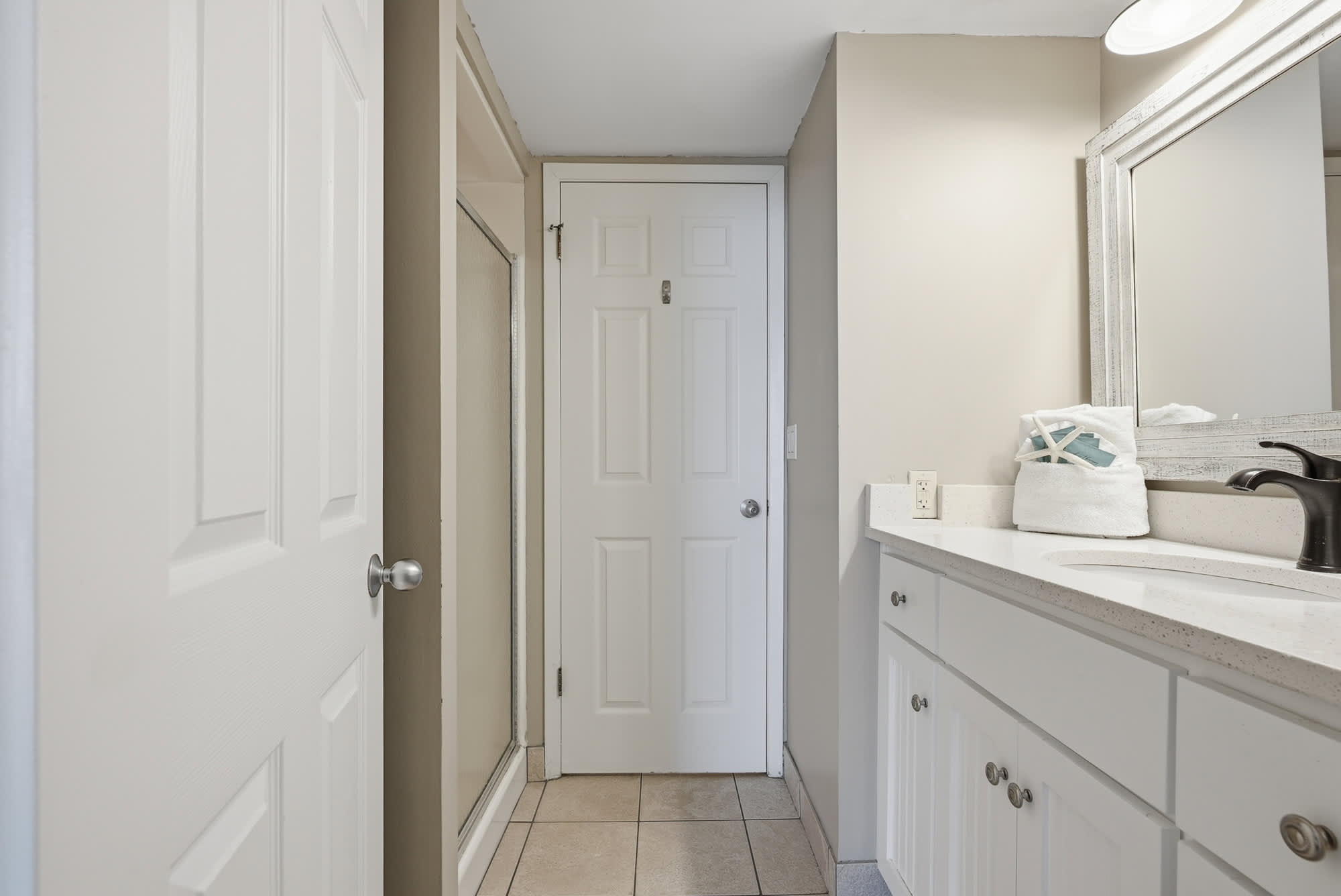 Dunes E1702 – Bathroom with white vanity, large mirror, and glass shower door.