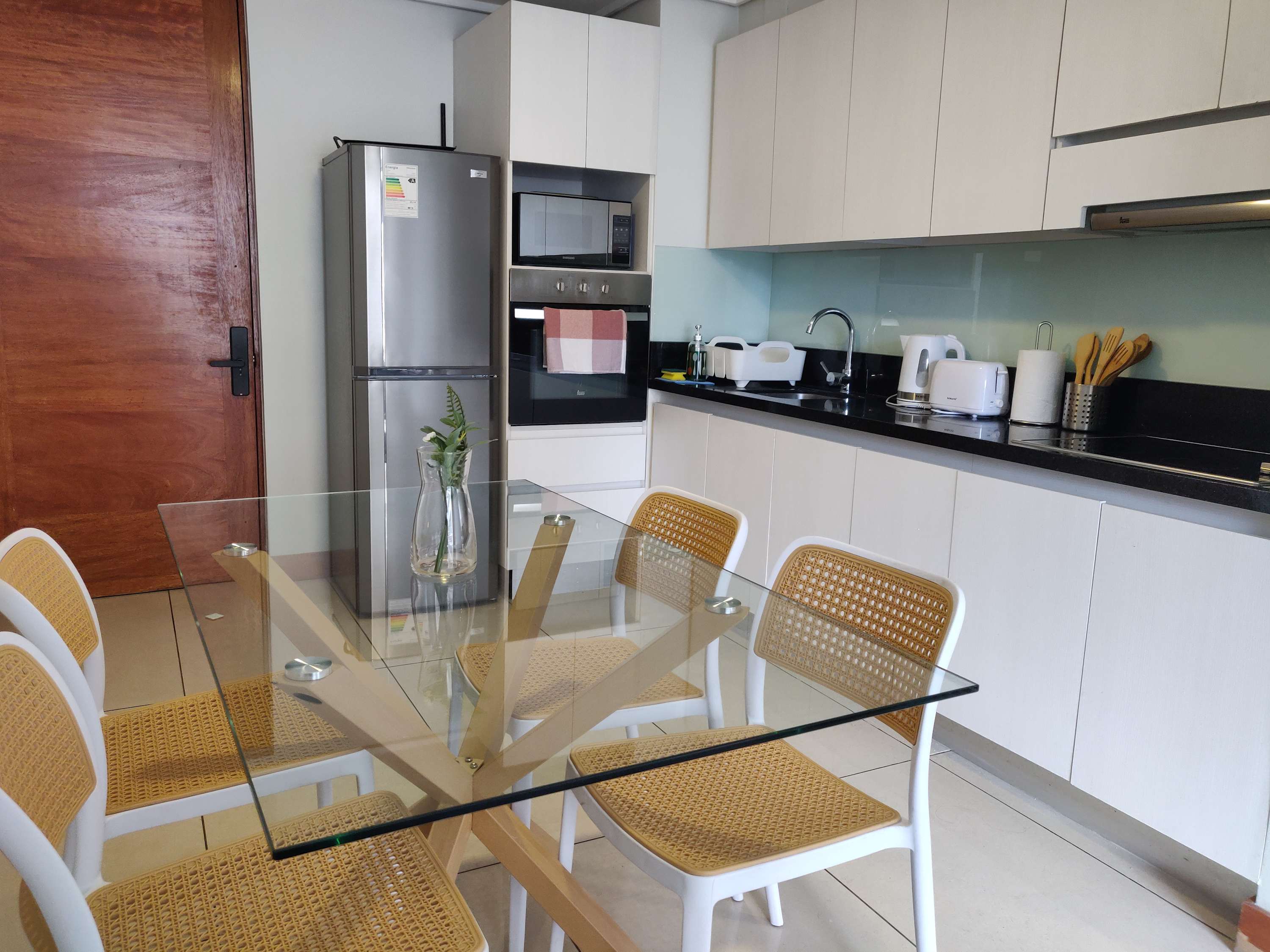 Sleek modern kitchen with glass dining table and stainless steel appliances, perfect for cozy meals.
