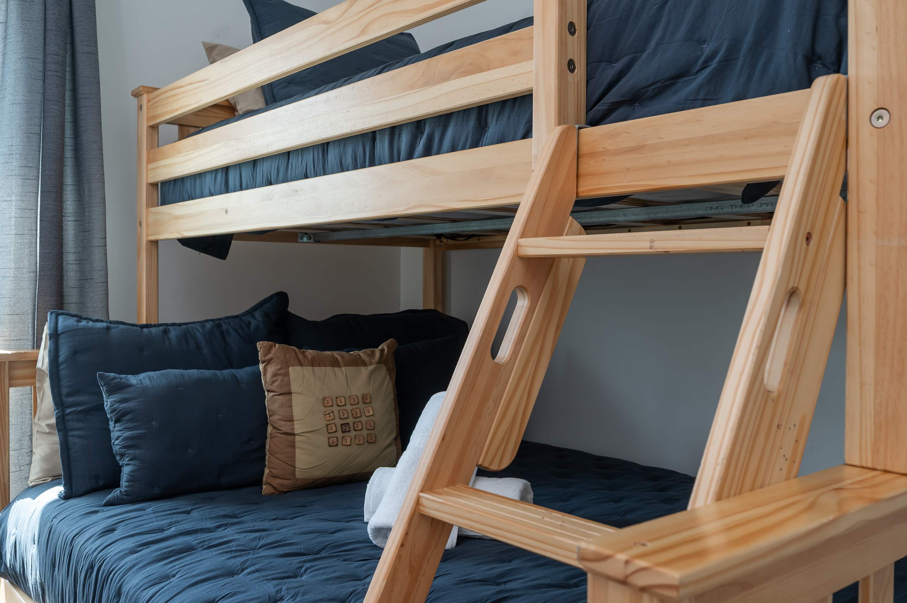 Sturdy wooden bunk bed with navy bedding and decorative pillows in a cozy room.
