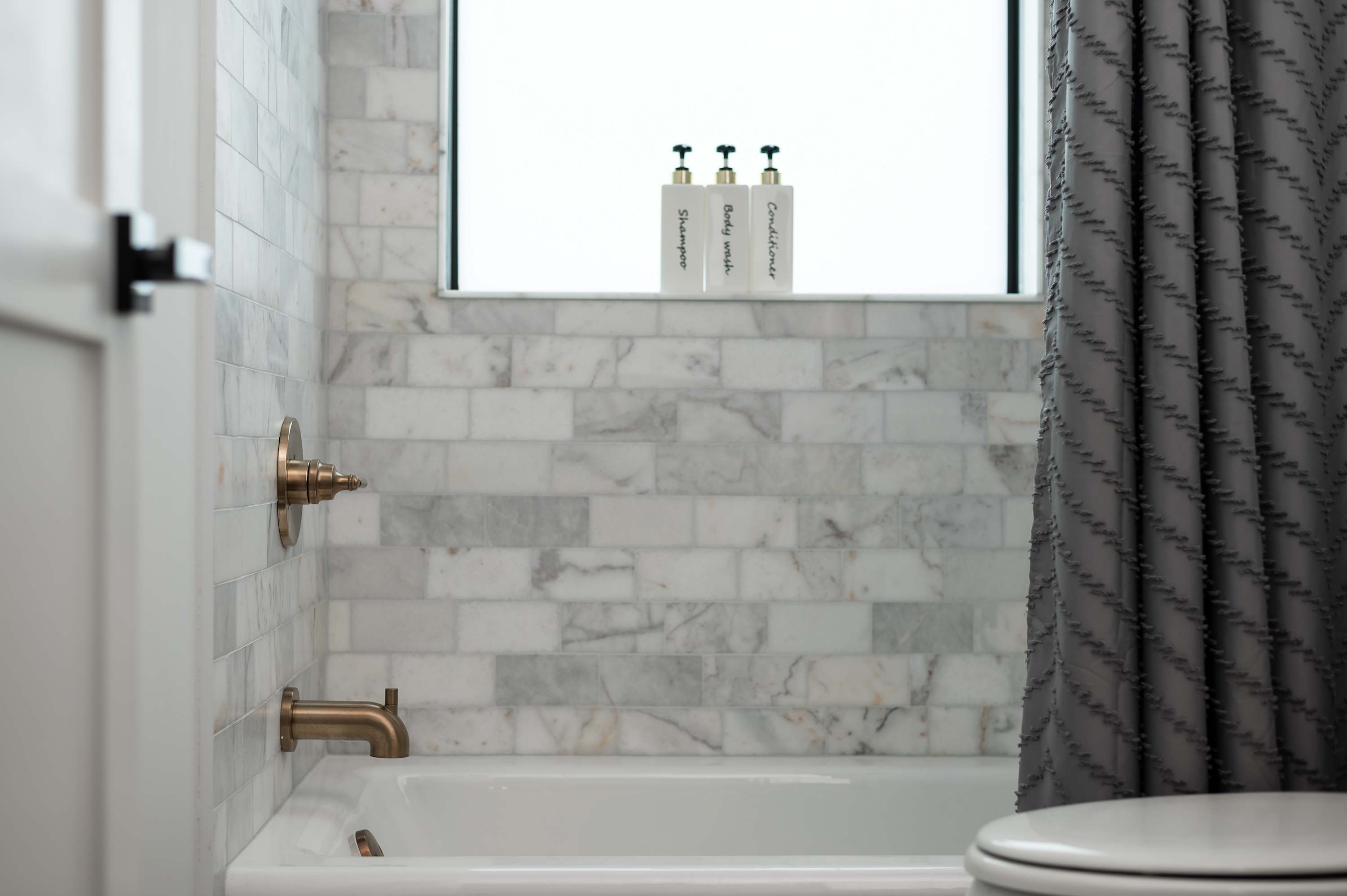 Marble-tiled bathtub area with bronze fixtures and a textured gray shower curtain.