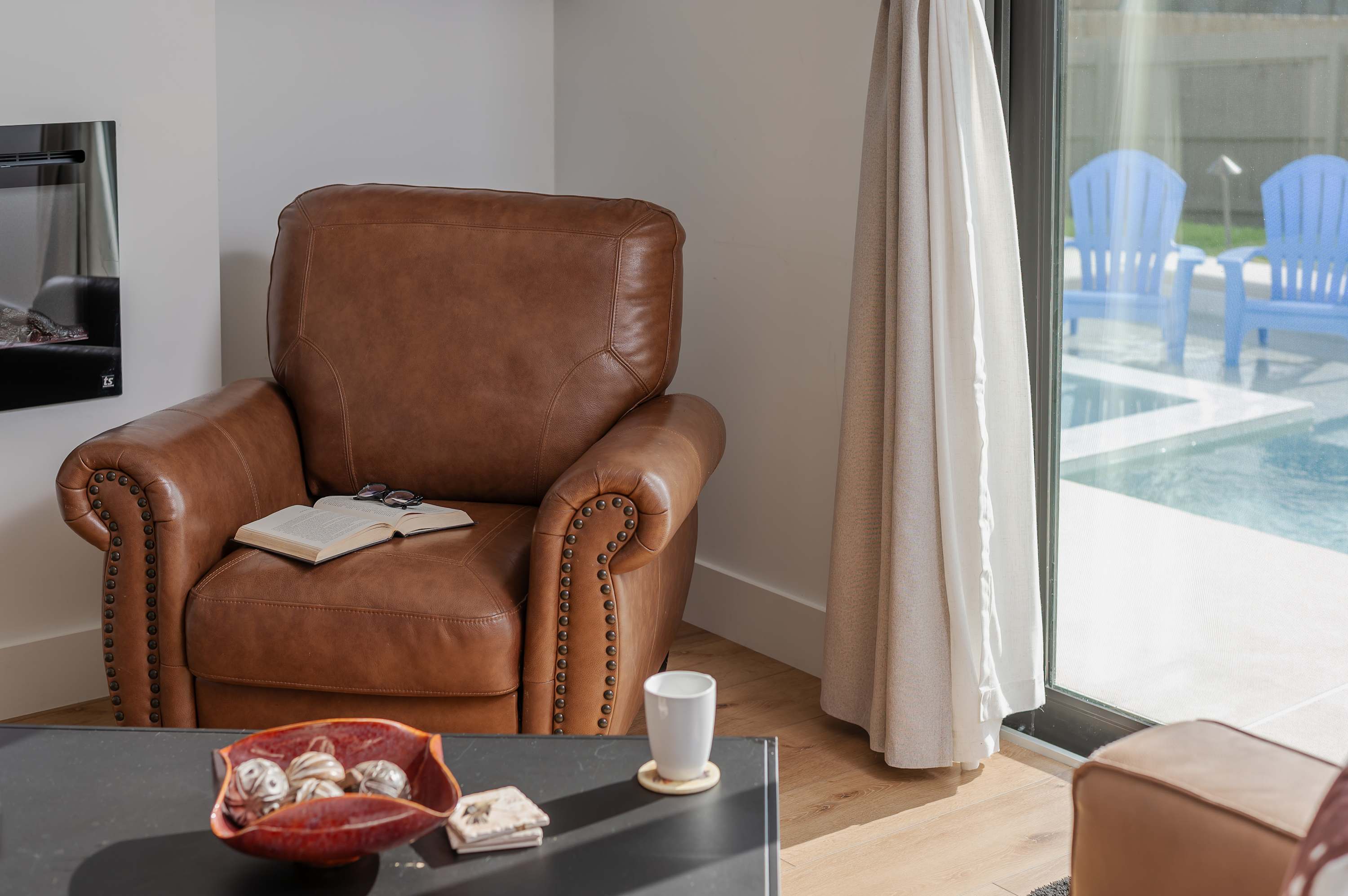 Cozy leather armchair next to a sliding door with a view of the pool and outdoor seating.