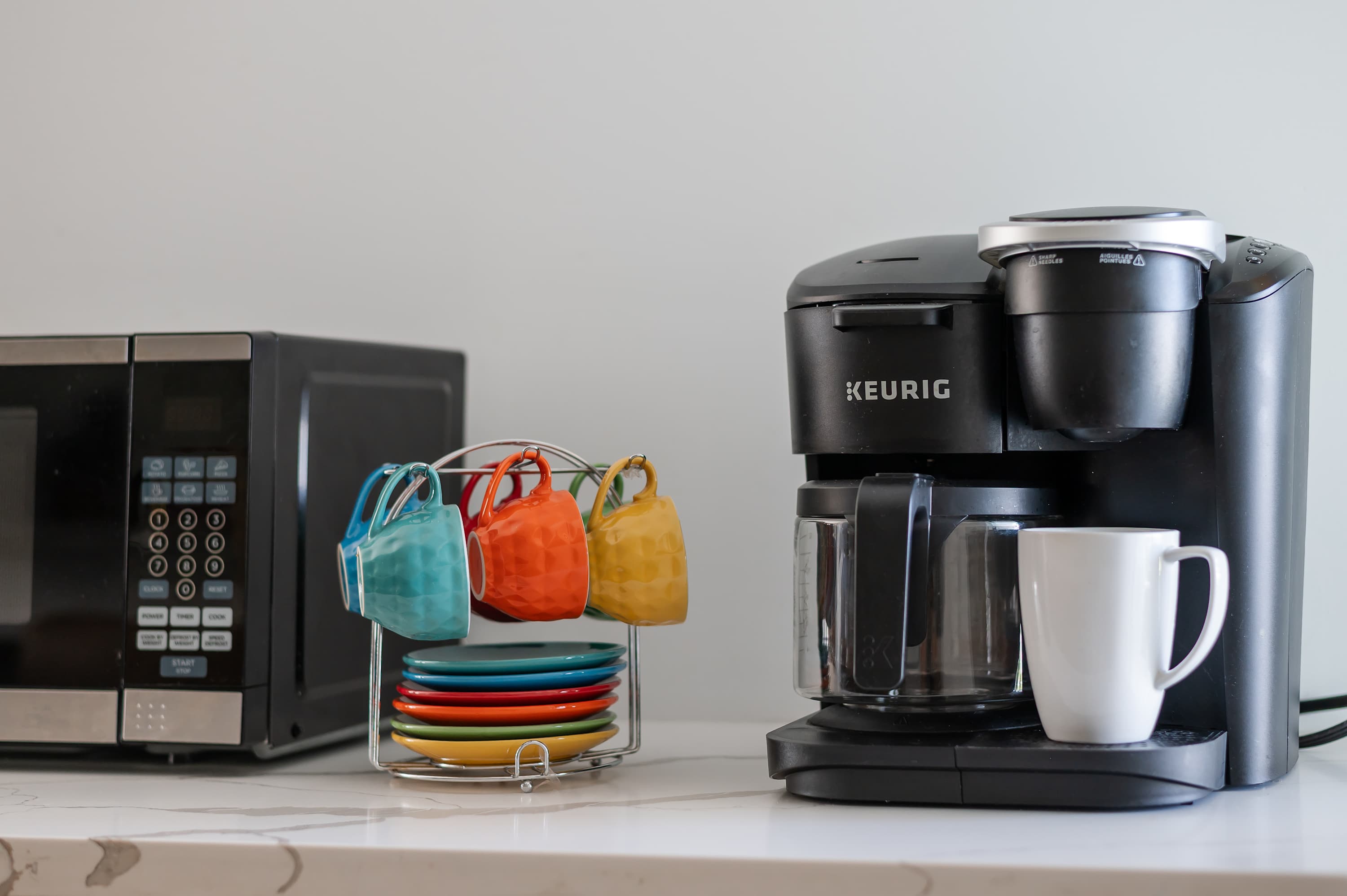 Modern kitchen counter with a coffee maker, microwave, and colorful mugs for a cozy start to your day.