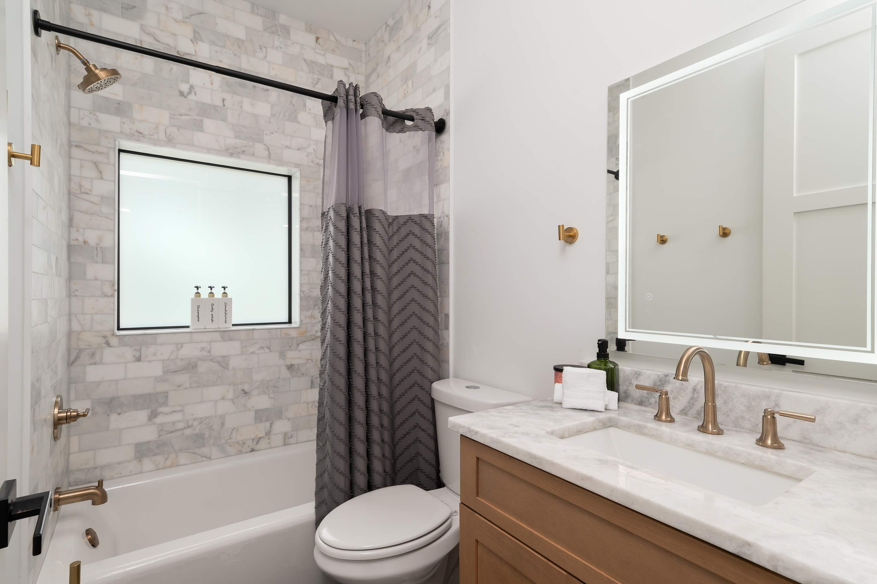 Modern bathroom featuring marble tile walls and a backlit mirror above the vanity.