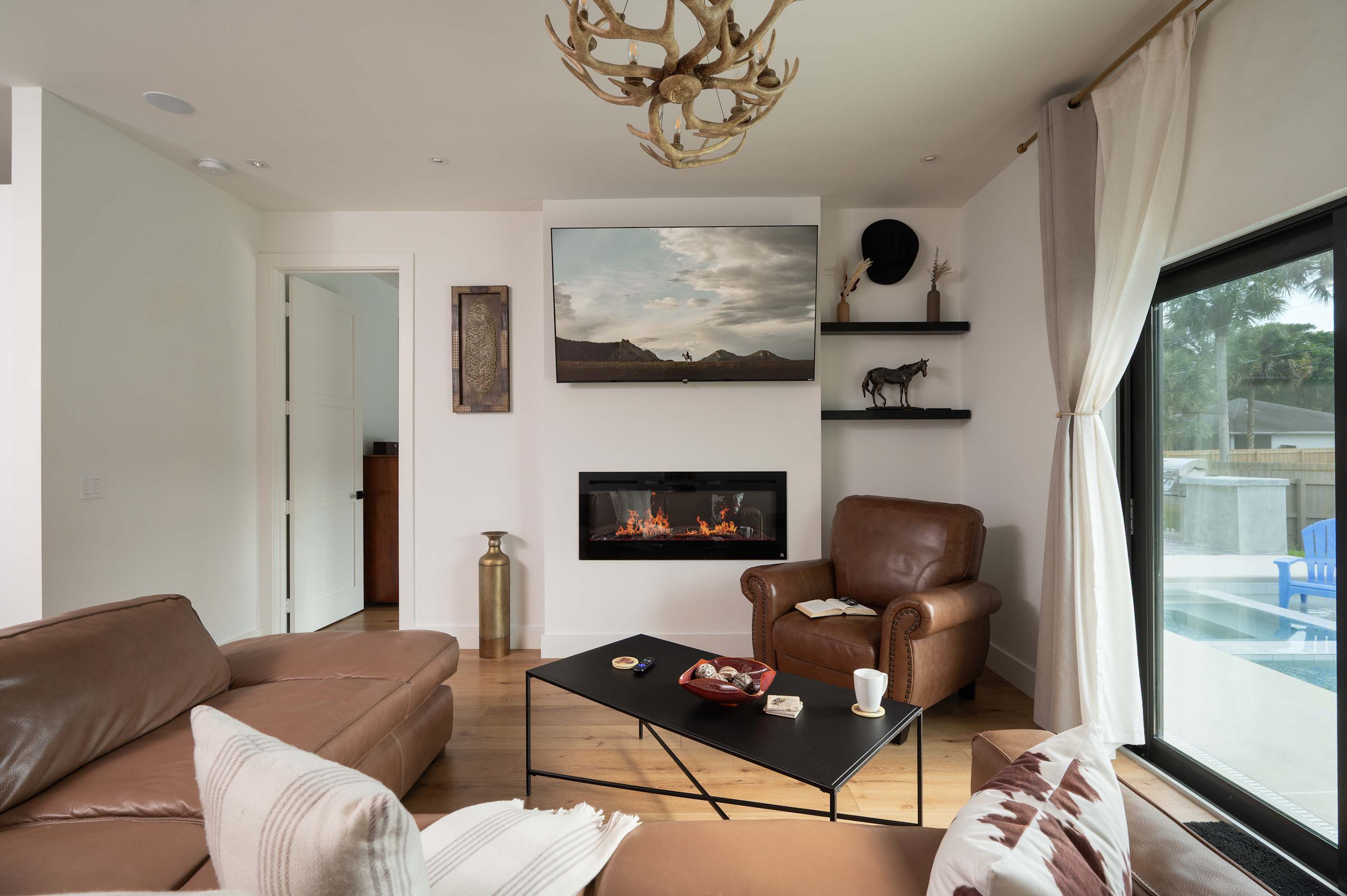 Cozy living room with leather seating, a modern fireplace, and a large window overlooking the pool.