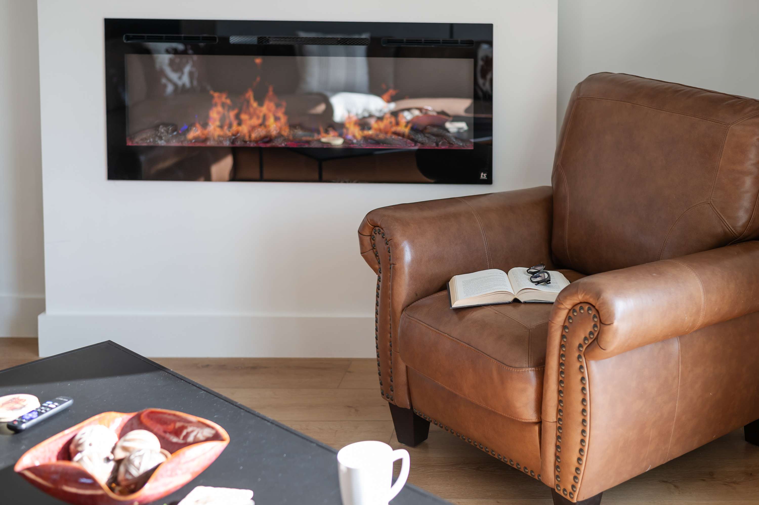Relax in the leather armchair by the modern electric fireplace with an open book and glasses.