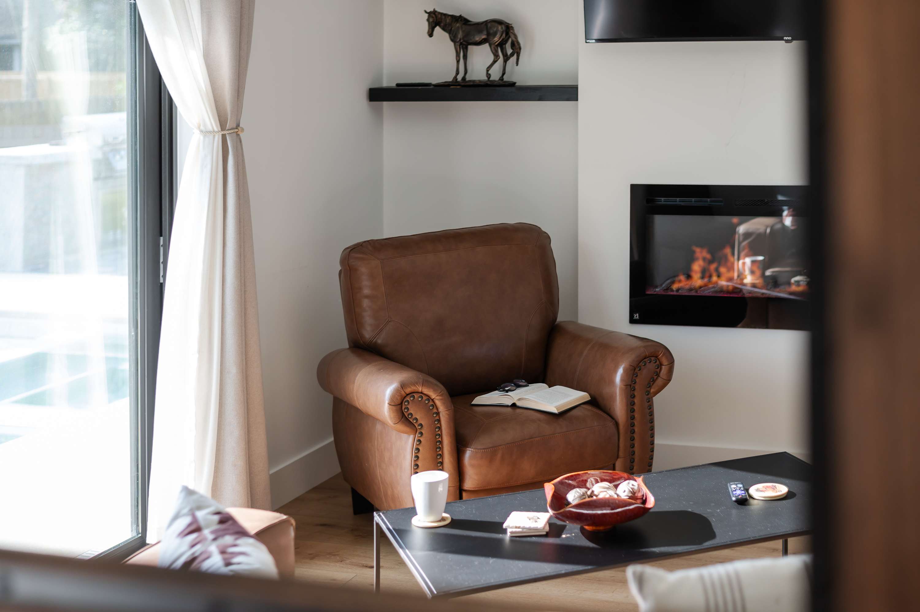 Cozy leather armchair next to a modern electric fireplace in a bright living room corner.