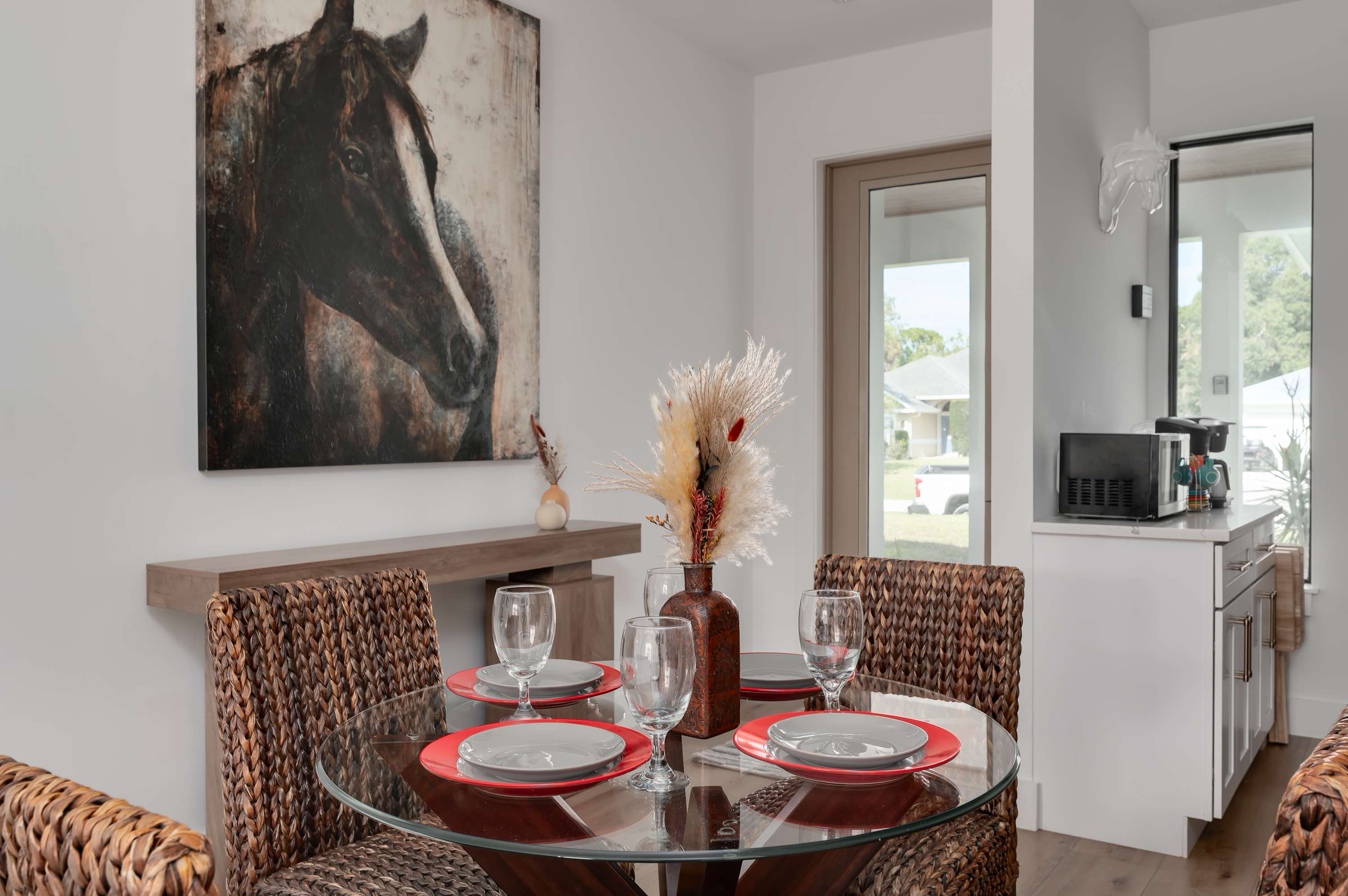 Dining area with woven chairs, glass table, and horse artwork in a modern setting