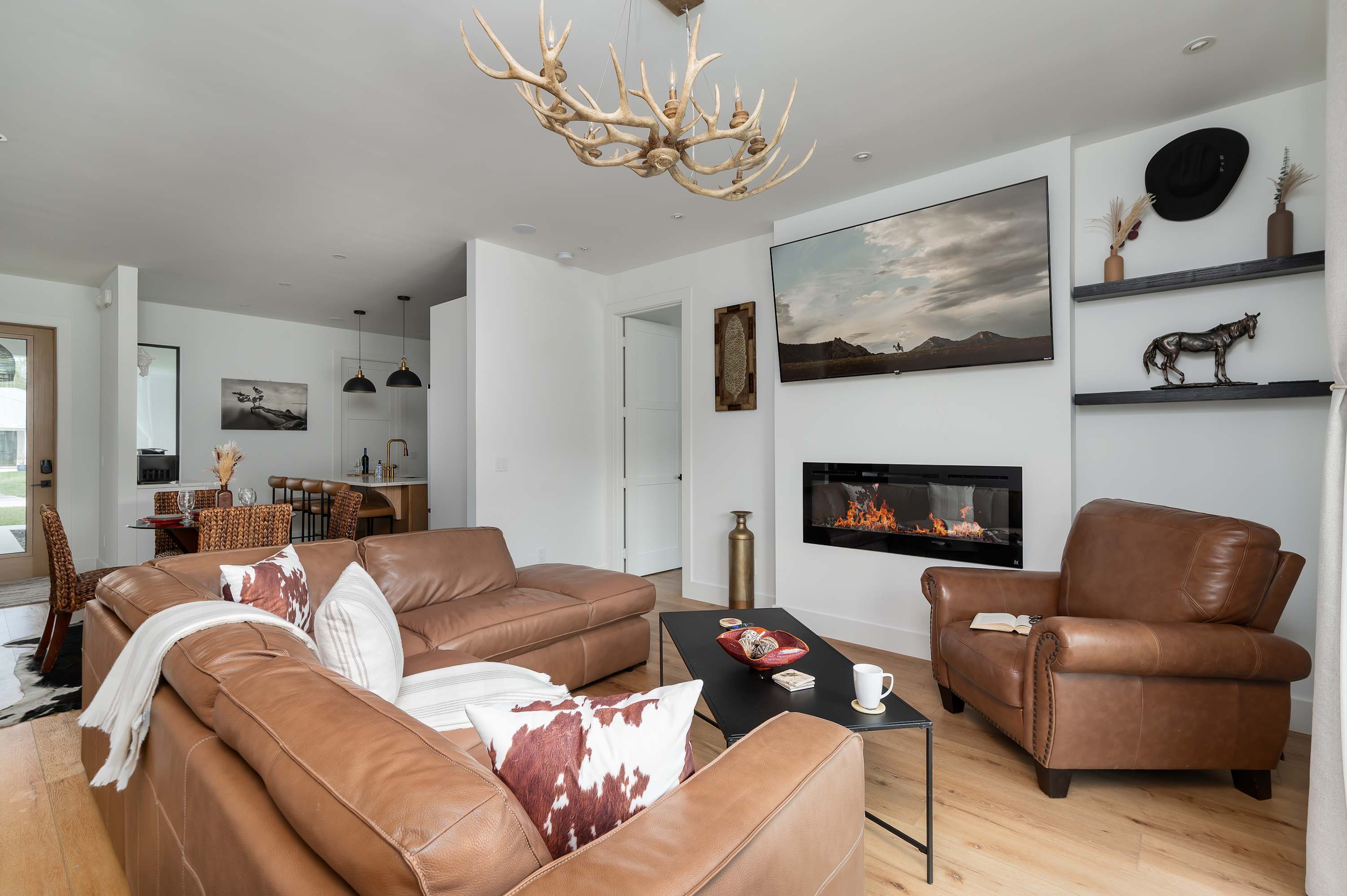 Modern living room with leather seating, a fireplace, and rustic antler chandelier.