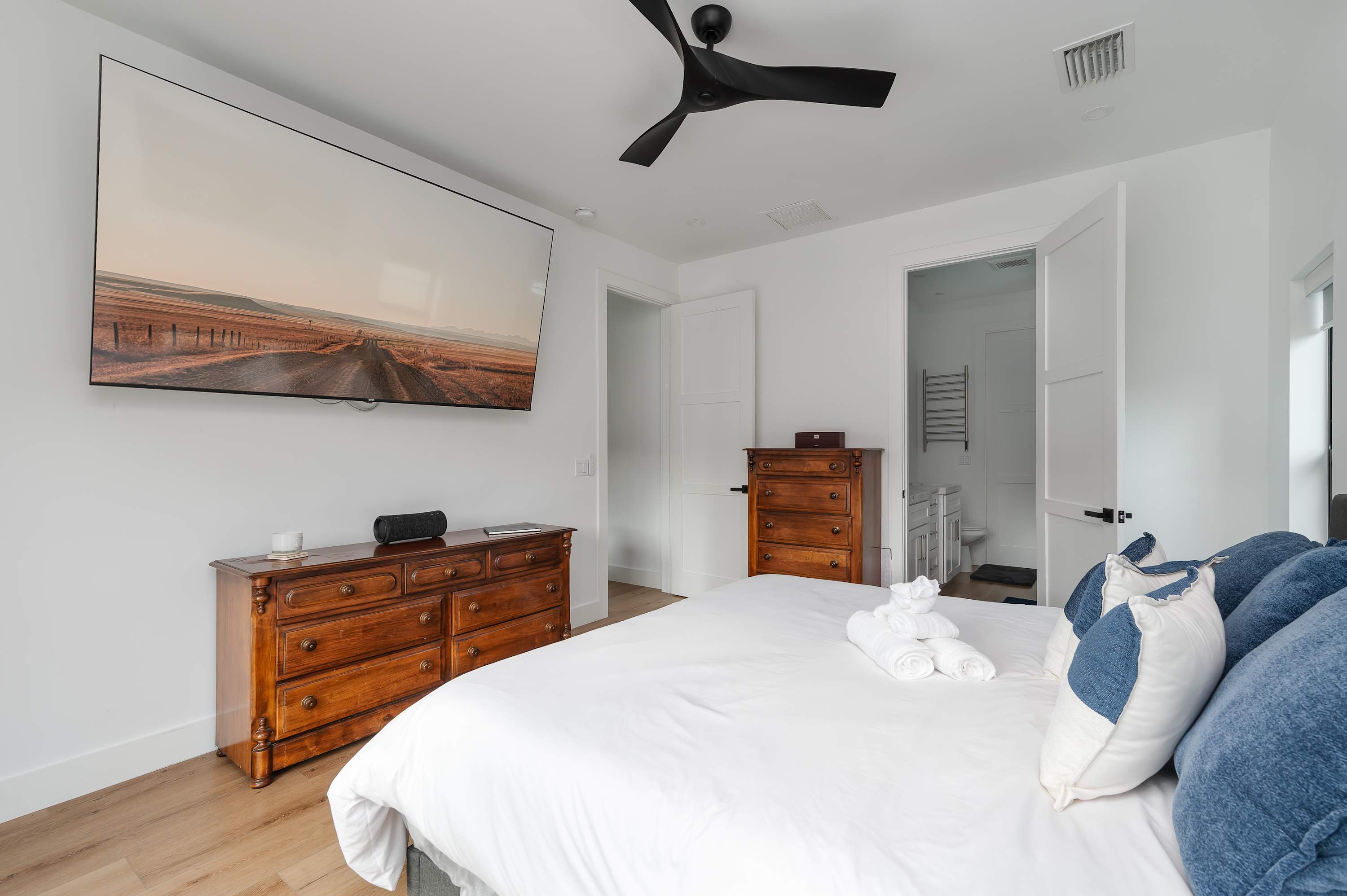 Modern bedroom featuring a large wall-mounted television and classic wooden dressers.