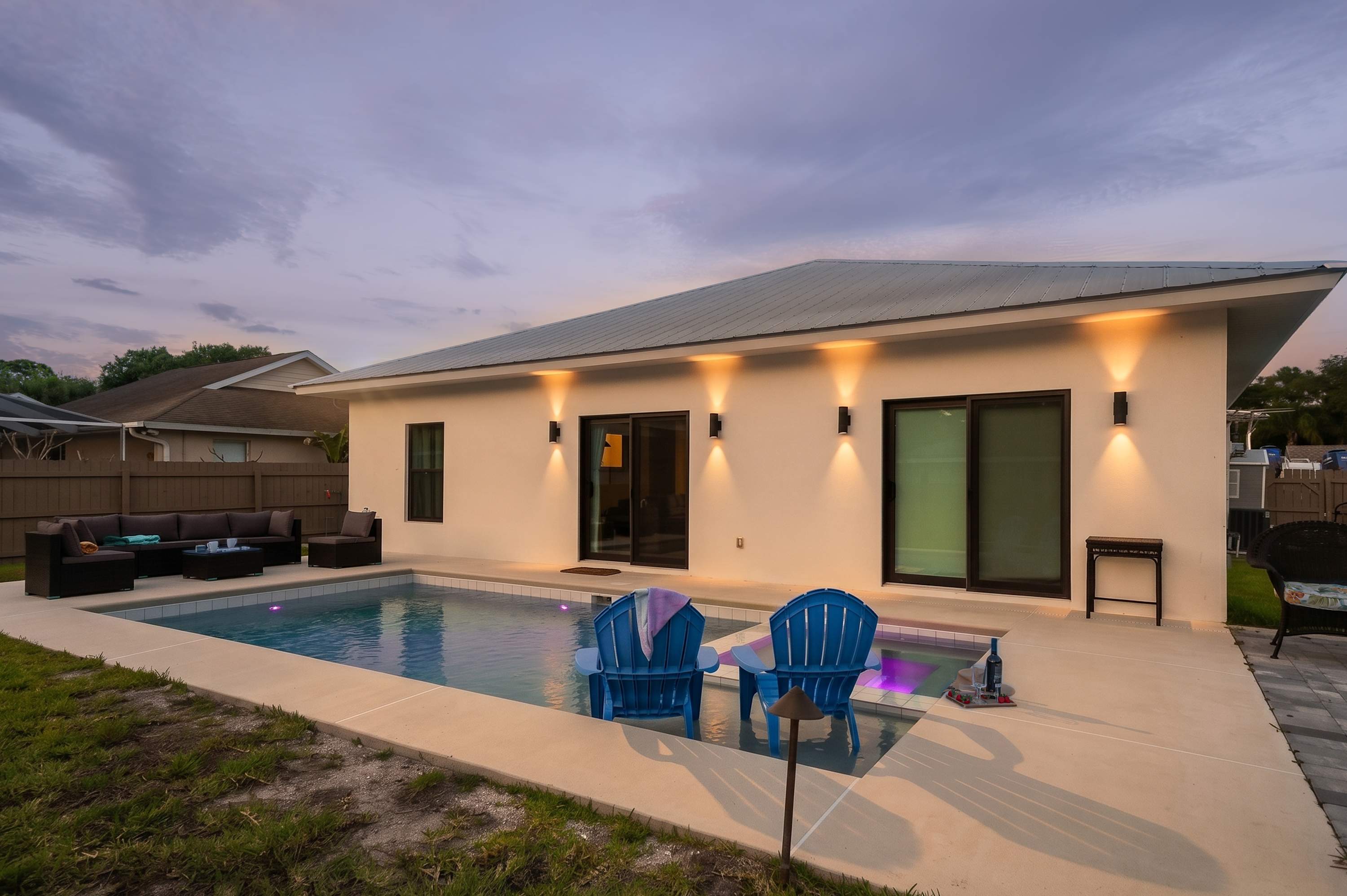 Modern backyard with a pool and outdoor seating area illuminated at dusk