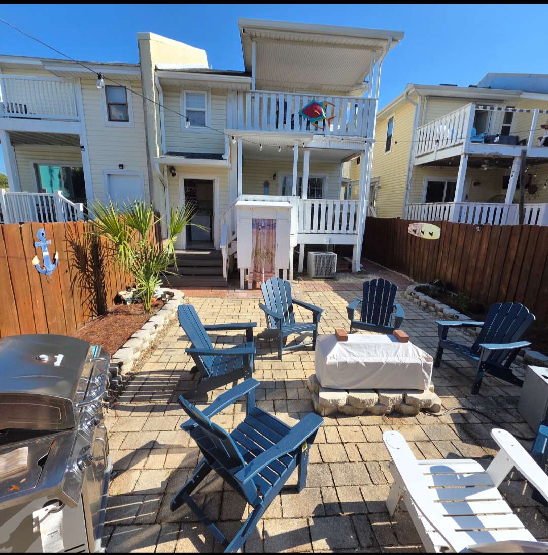 7405 Beach Dr A – Patio area with blue lounge chairs, fire pit, and a grill near a two-story beach house.