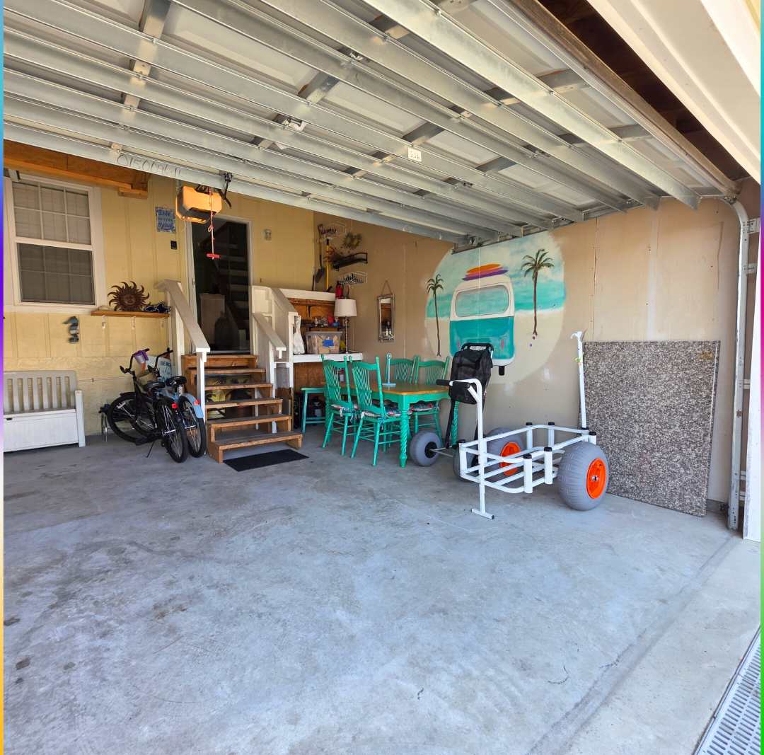 7405 Beach Dr A – Garage space featuring bicycles, a dining table with teal chairs, and steps leading to an upper level.