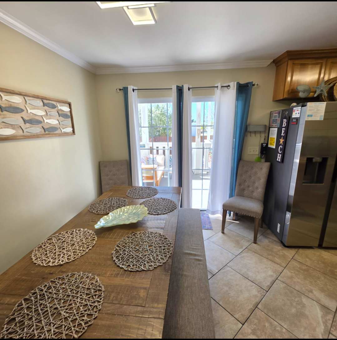 7405 Beach Dr A – Bright dining area with a wooden table, six placemats, and views through sliding glass doors.