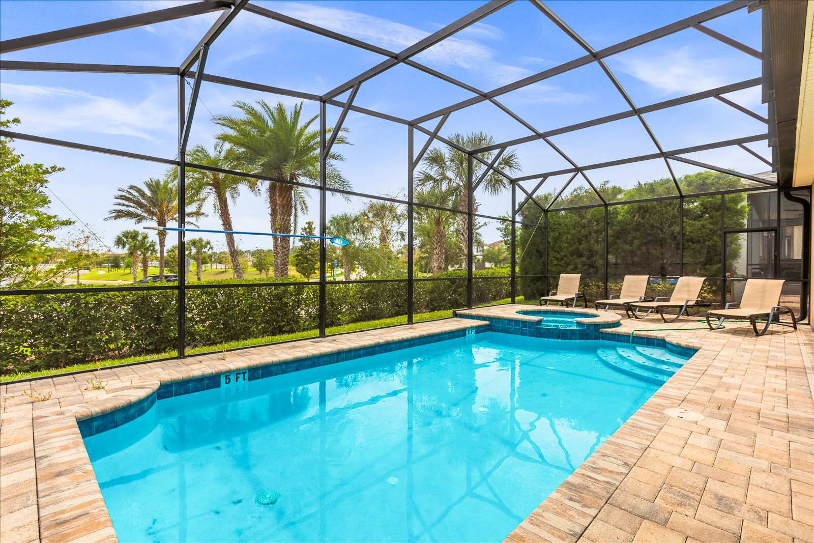 Private screened pool and spa with four loungers, tropical palms, and a sunny landscaped view—an inviting outdoor retreat for relaxing and swimming.