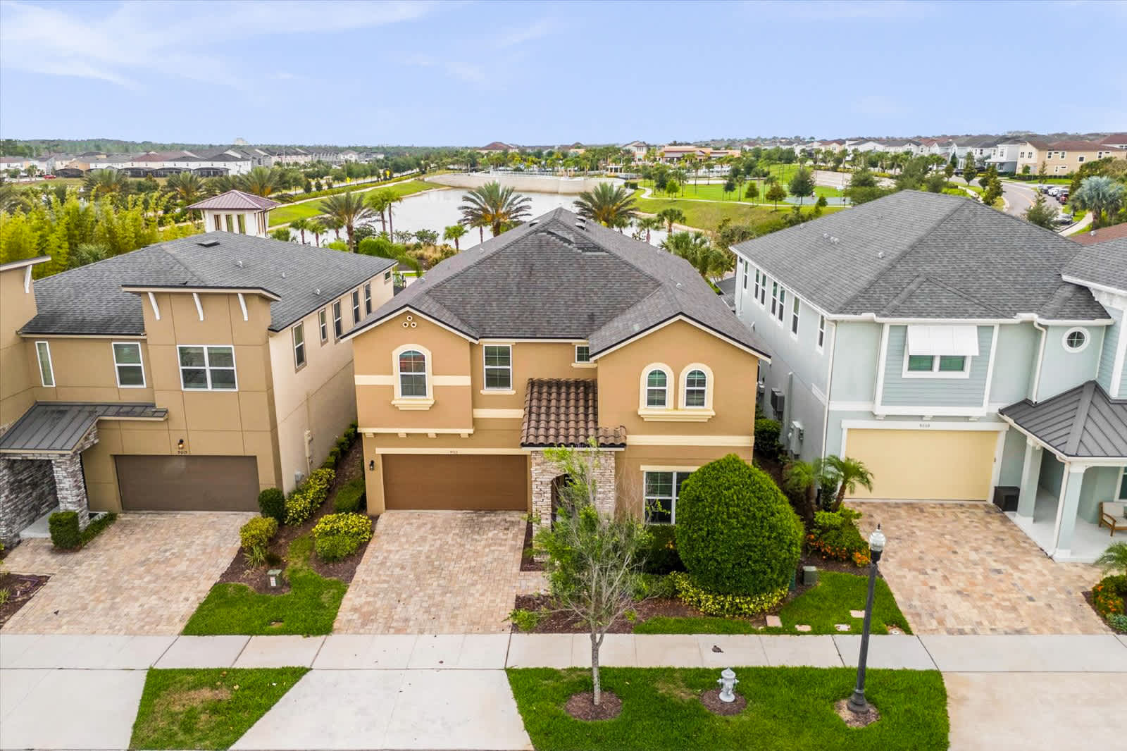 Aerial view of the spacious villa, featuring arched windows, stone accents, manicured landscaping, and a scenic community pond beyond.