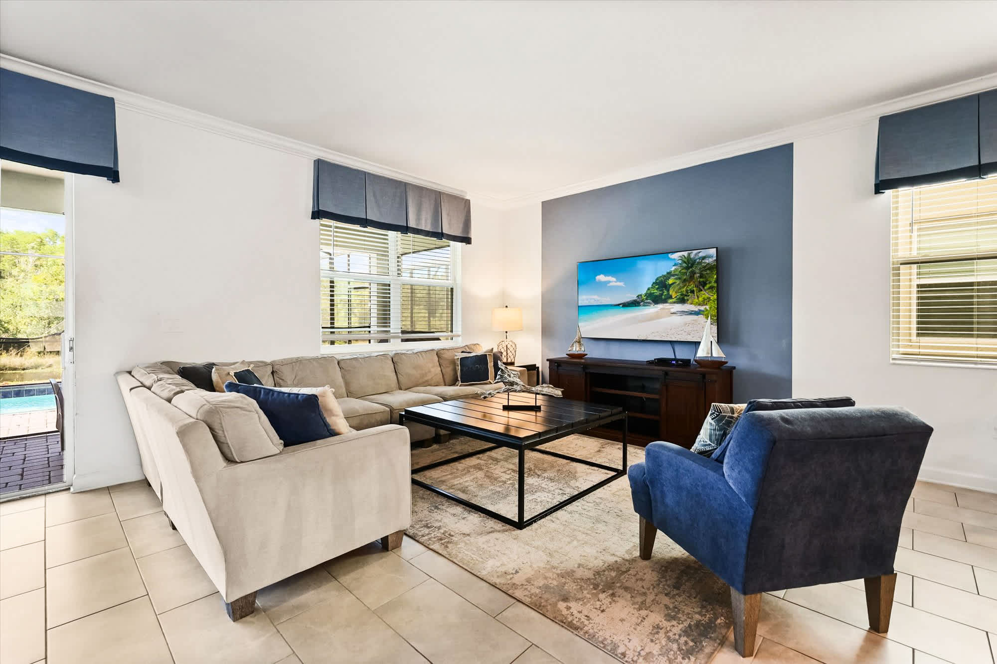 Relax in this spacious living room with a plush sectional, vibrant decor, and pool views, perfect for unwinding.